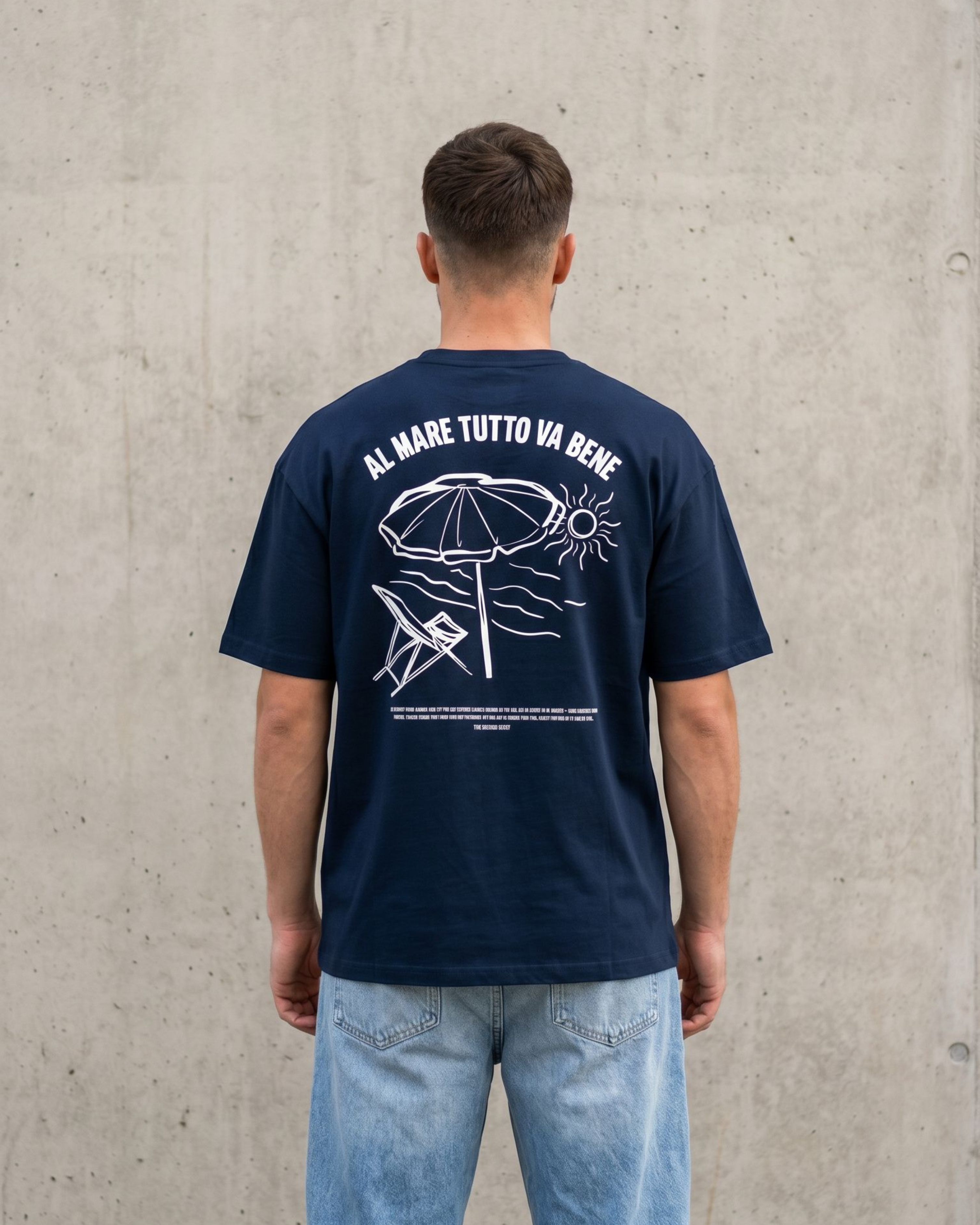 Person wearing a navy blue t-shirt with white graphics and text, standing against a concrete wall.