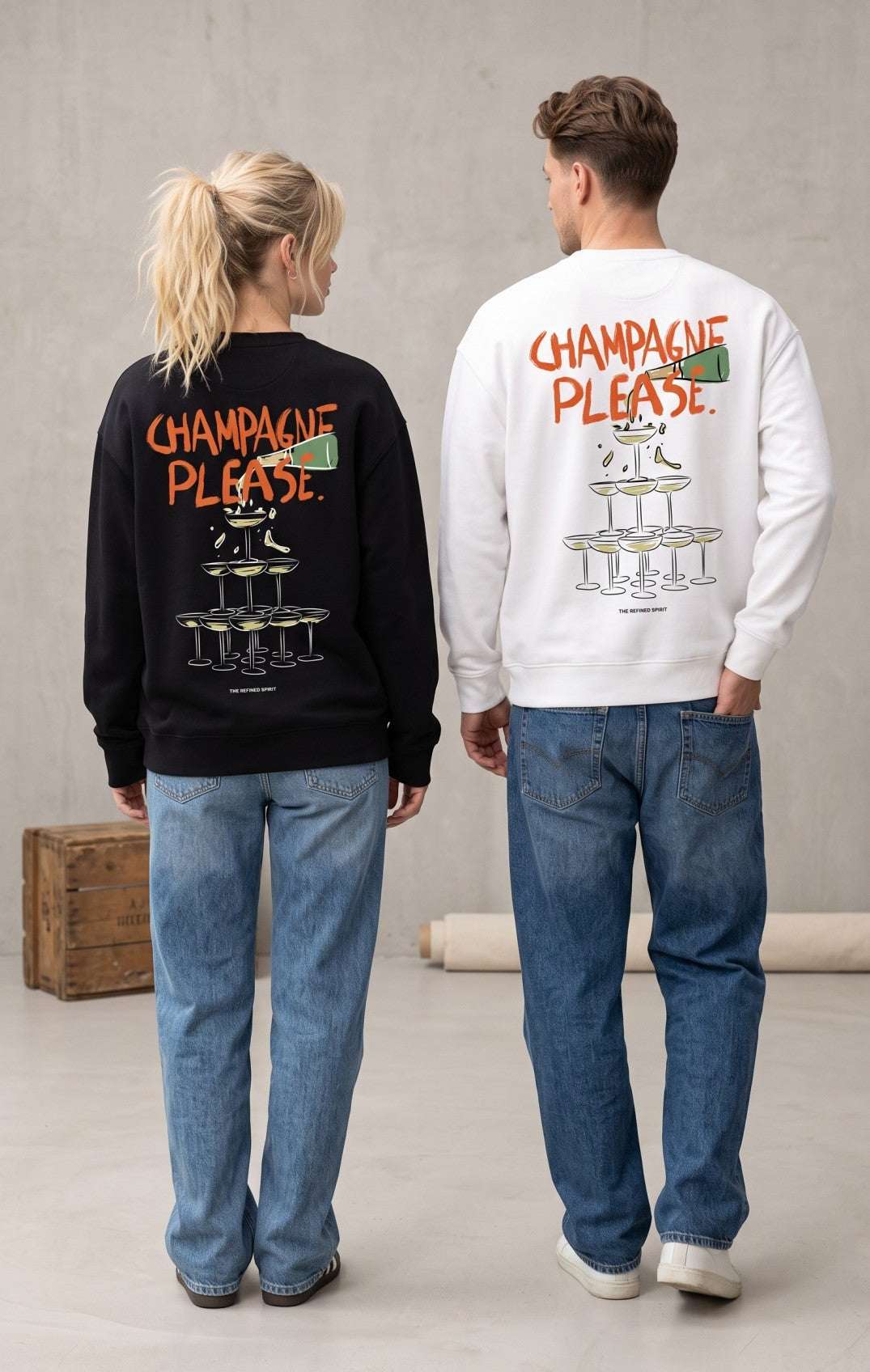 Two models shown from behind wearing matching sweatshirts with 'CHAMPAGNE PLEASE' and a champagne tower graphic printed on the back, one in black and one in white, paired with blue jeans in a studio setting.