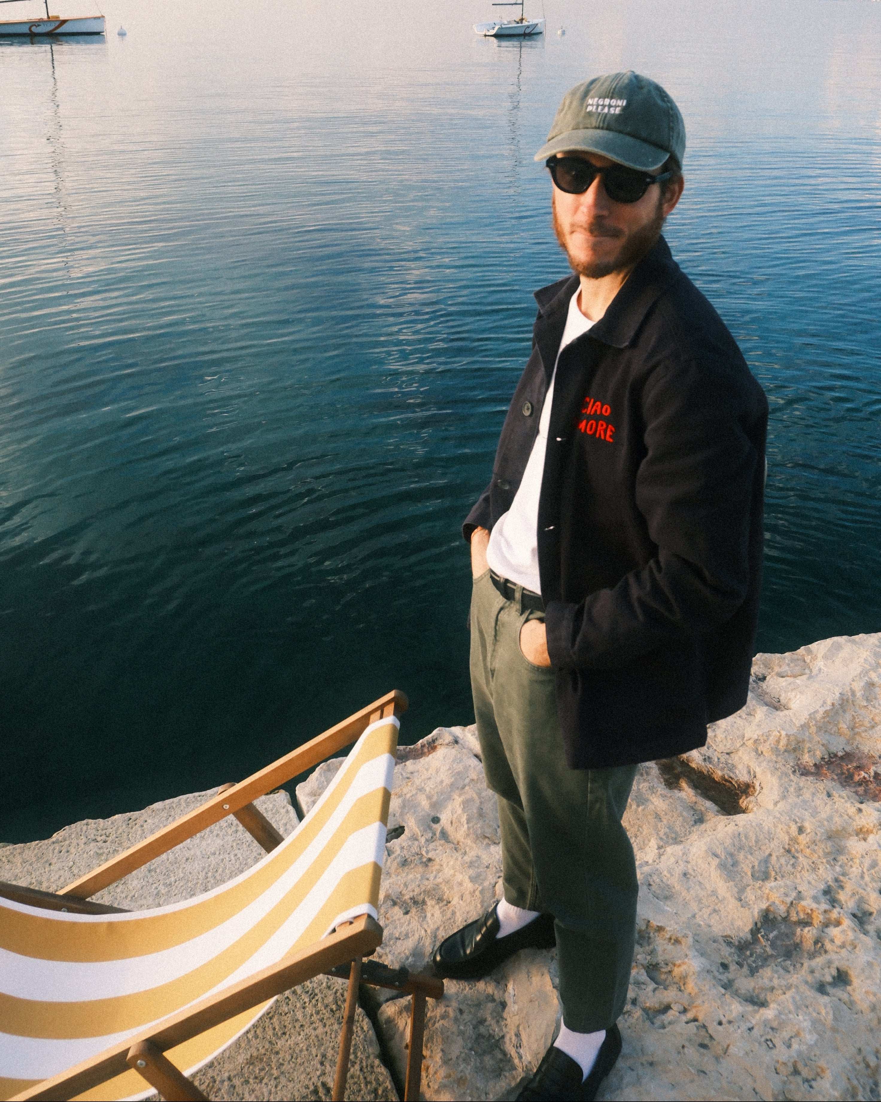Person standing by a body of water with a striped chair in the background