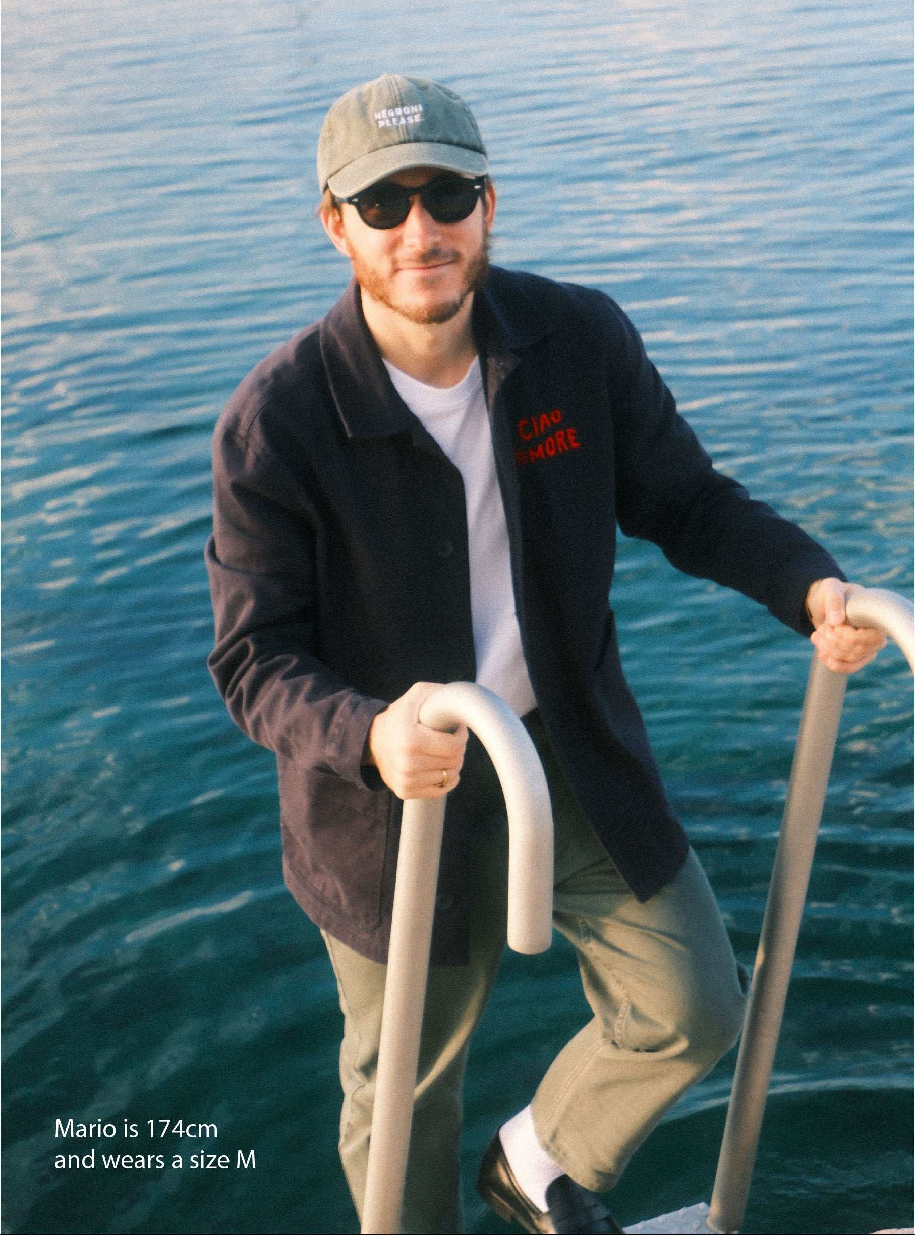 Man on a boat in the water wearing sunglasses and a cap.