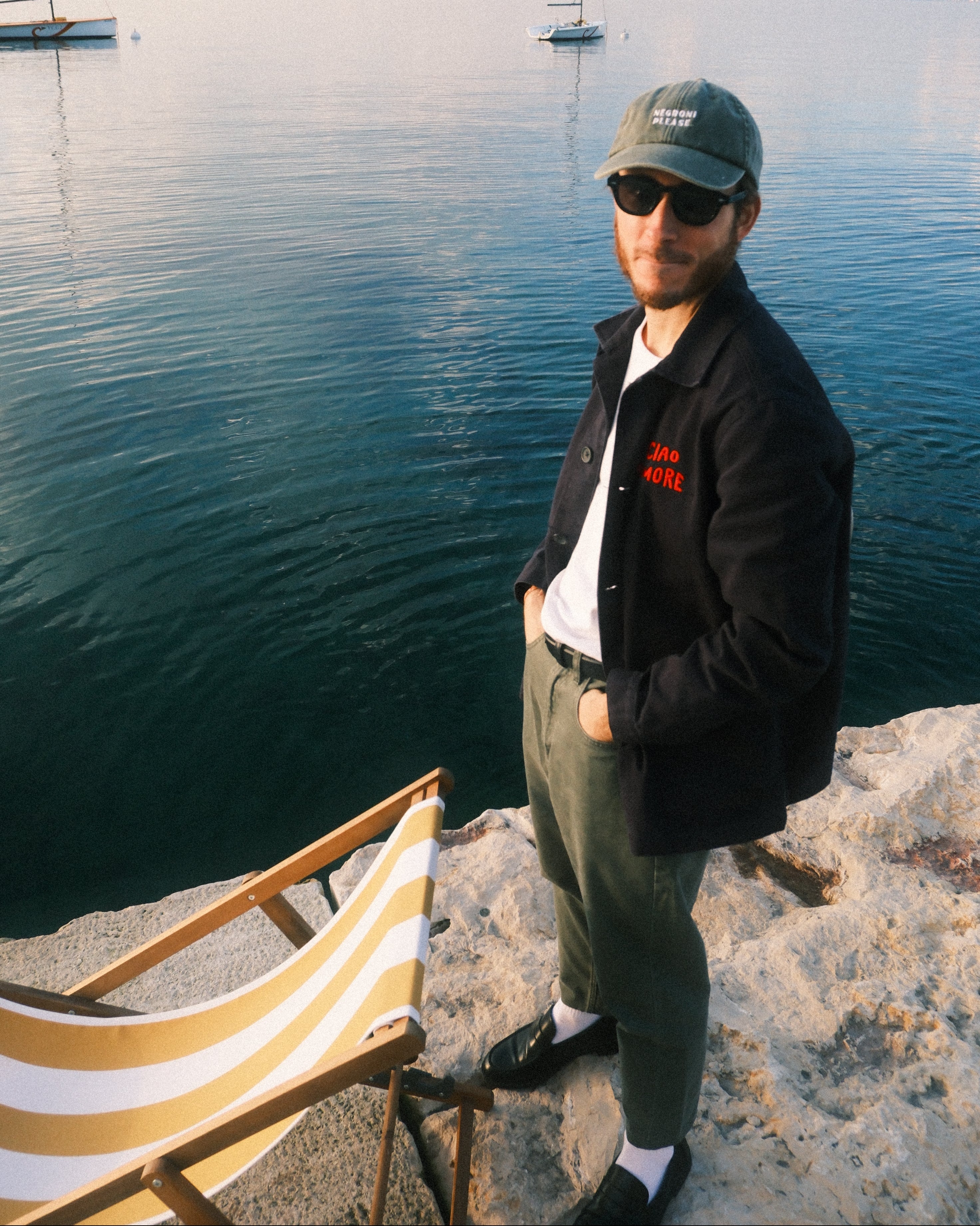 Person standing by a body of water with a striped chair in the background
