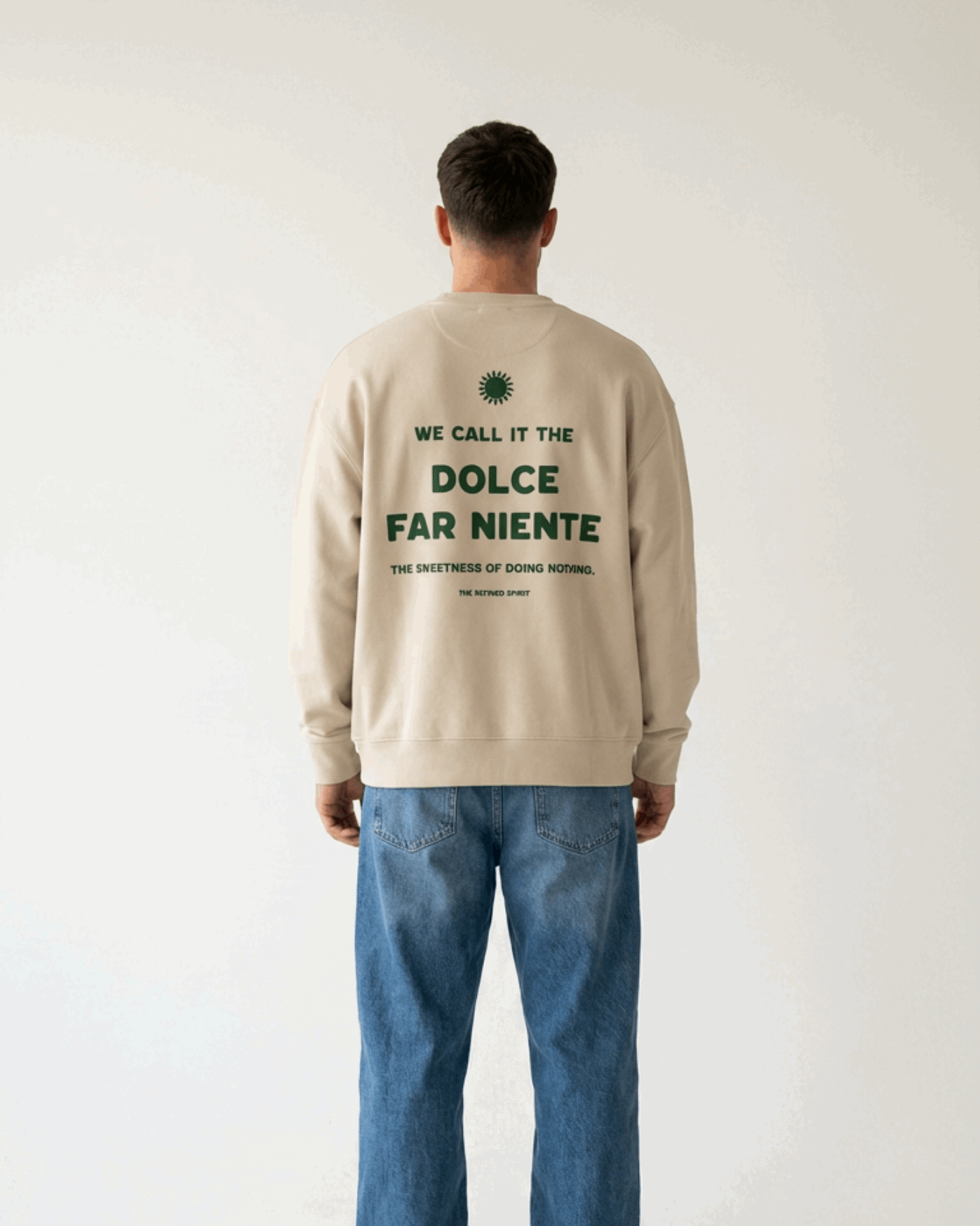 Person wearing a beige sweatshirt with text on the back, standing against a plain background