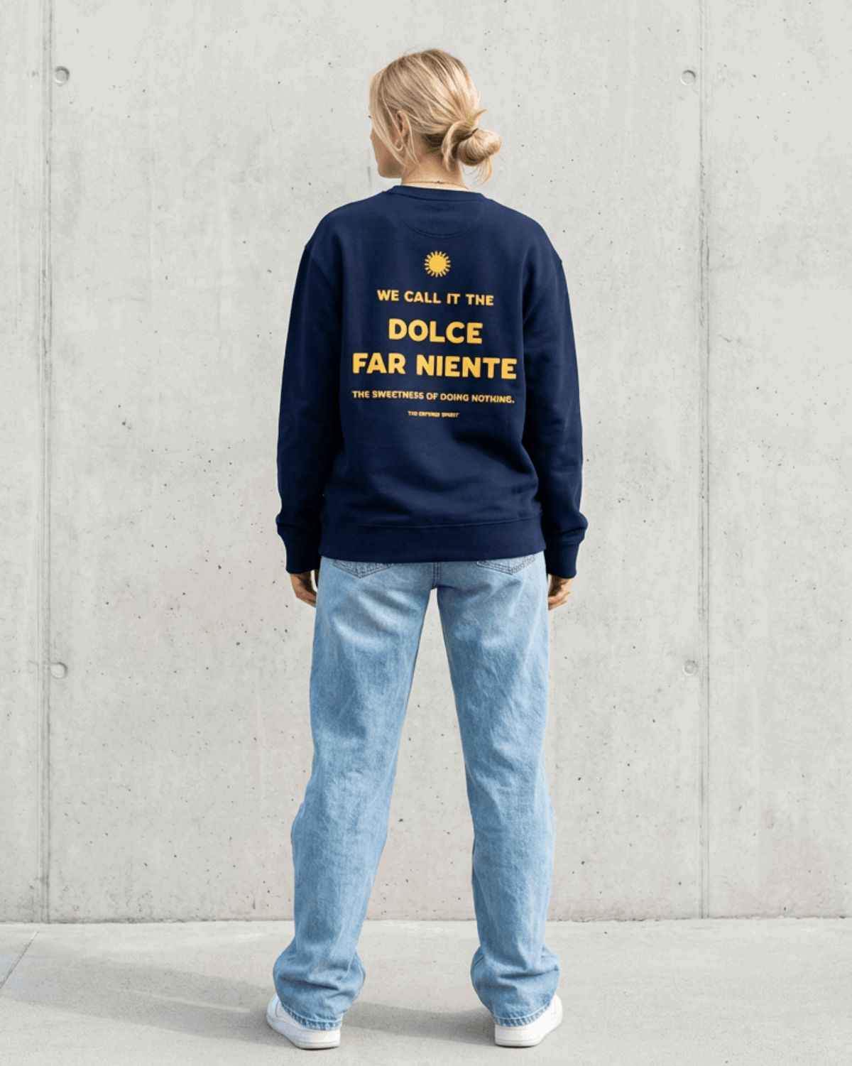 Person wearing a navy sweatshirt with text on the back against a light gray wall.