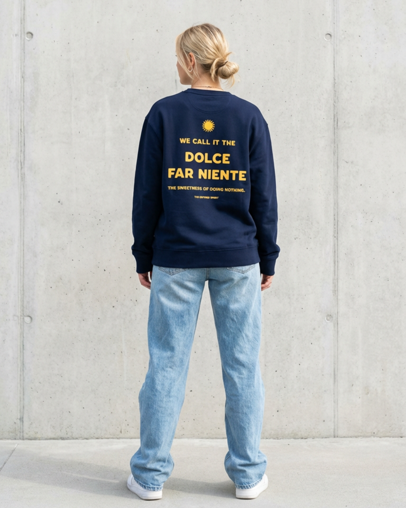 Person wearing a navy sweatshirt with text on the back against a light gray wall.