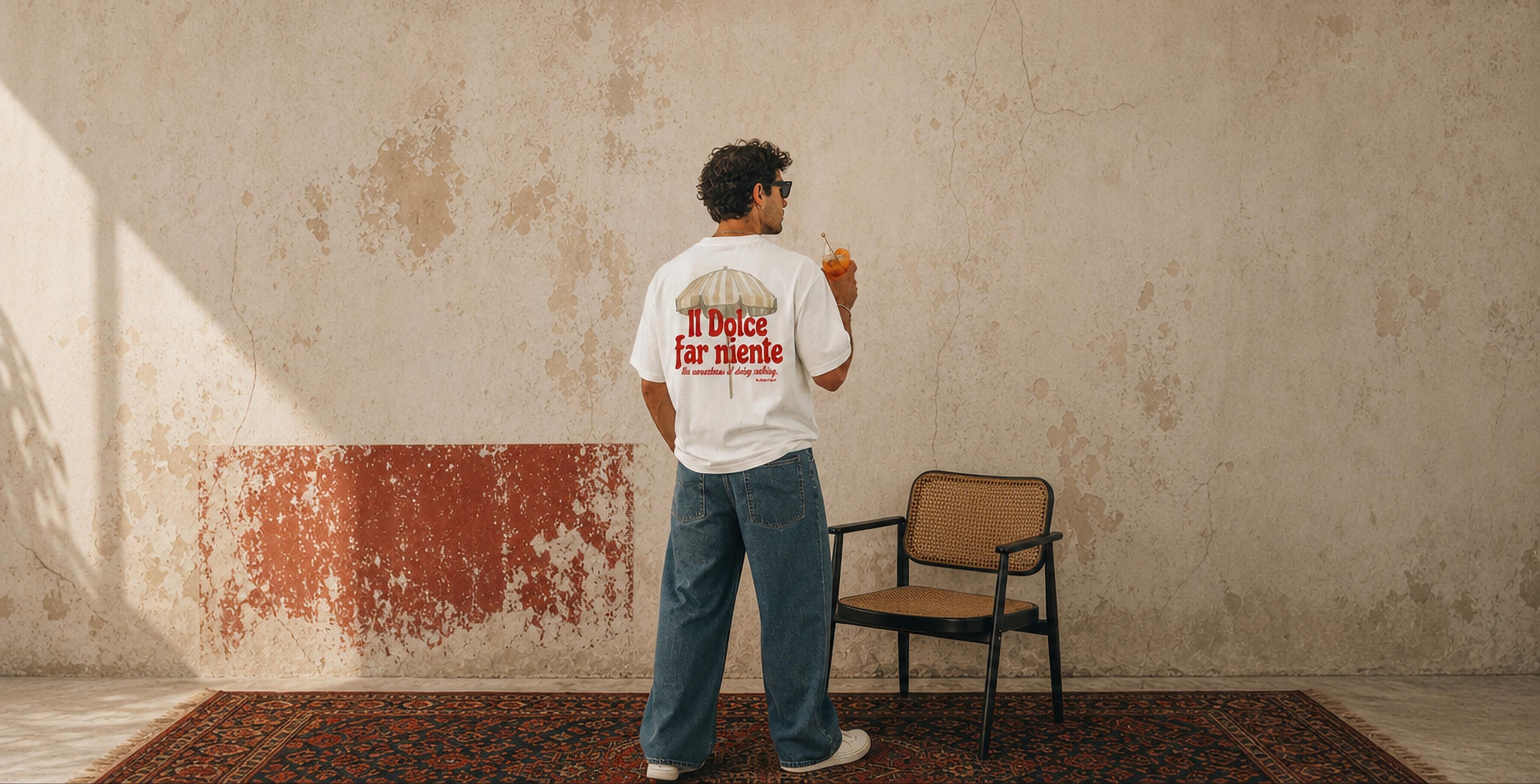 Person wearing a white t-shirt with text standing in a room with a chair and rug.