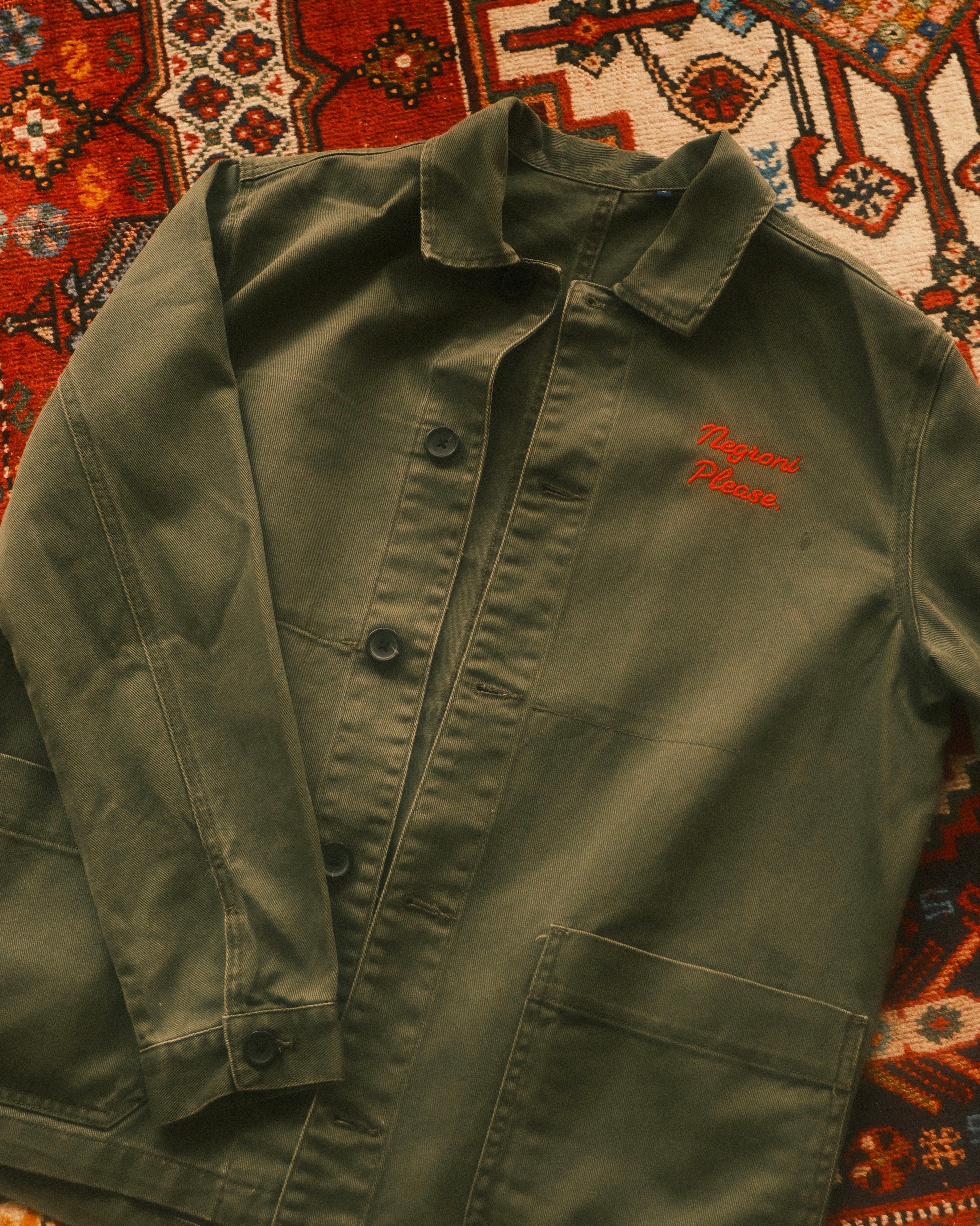 Green jacket with red text on a patterned rug