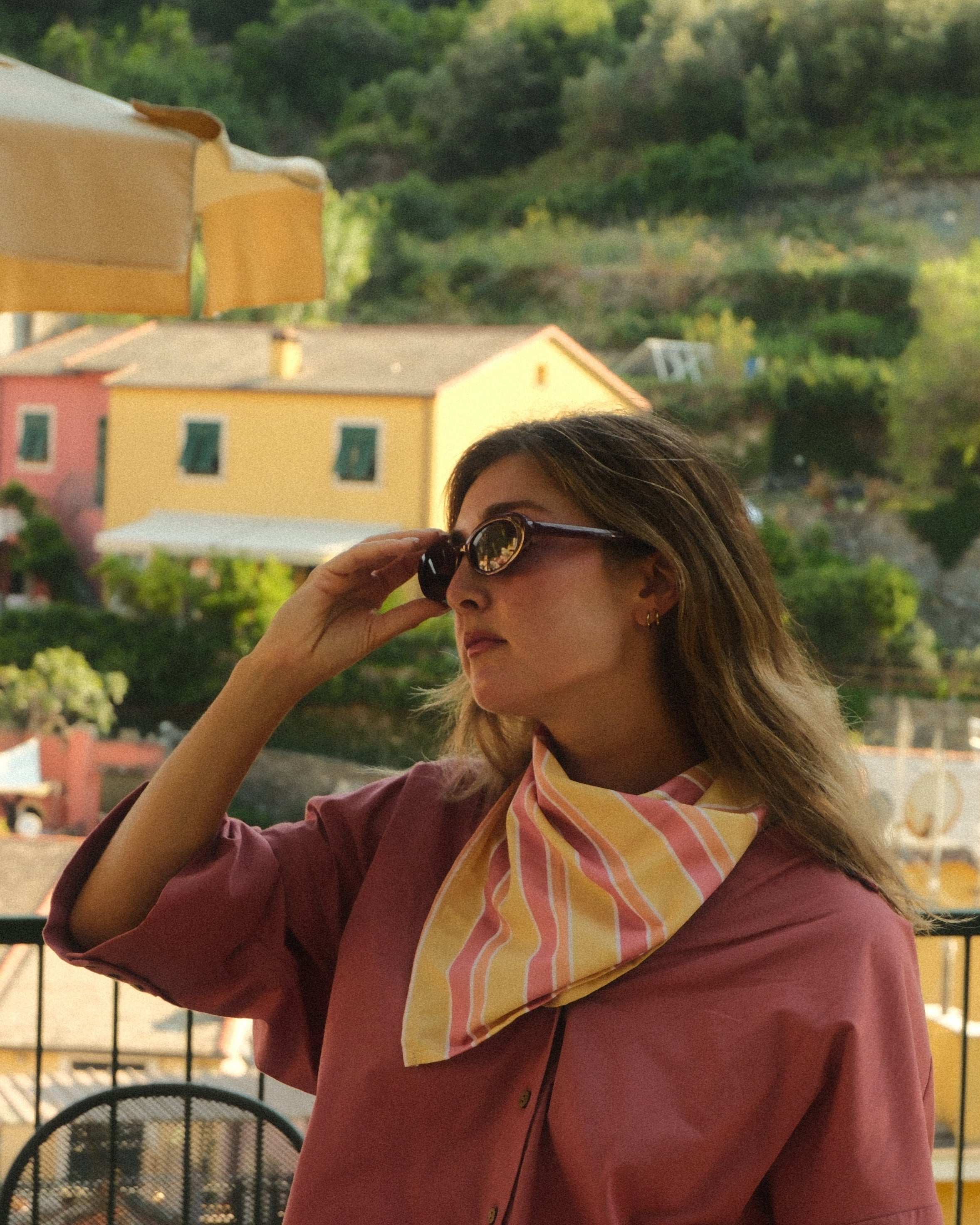 Woman standing on a balcony with a scenic view of colorful buildings and greenery.