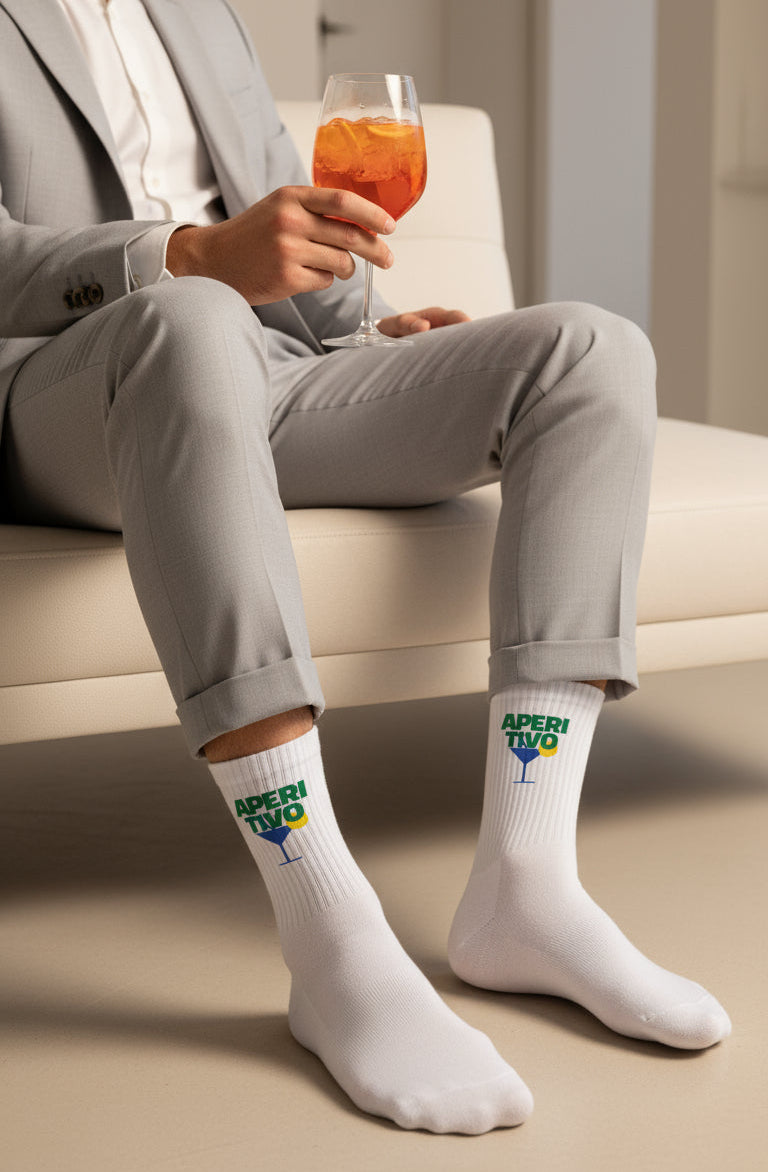 Man in gray suit sitting on a couch wearing white socks with Aperol logo, holding a glass of Aperol cocktail.
