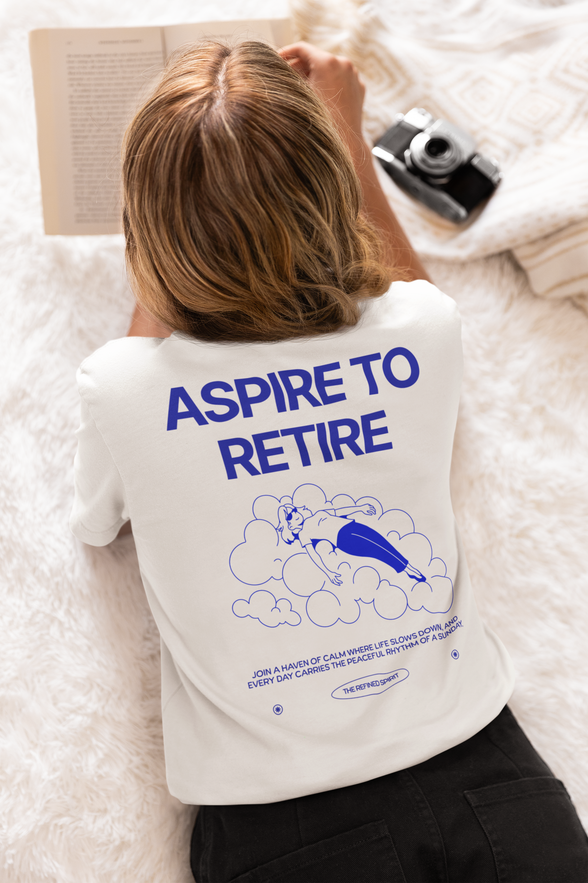 Person wearing a white t-shirt with 'Aspire to Retire' text and graphic on a fluffy white surface.