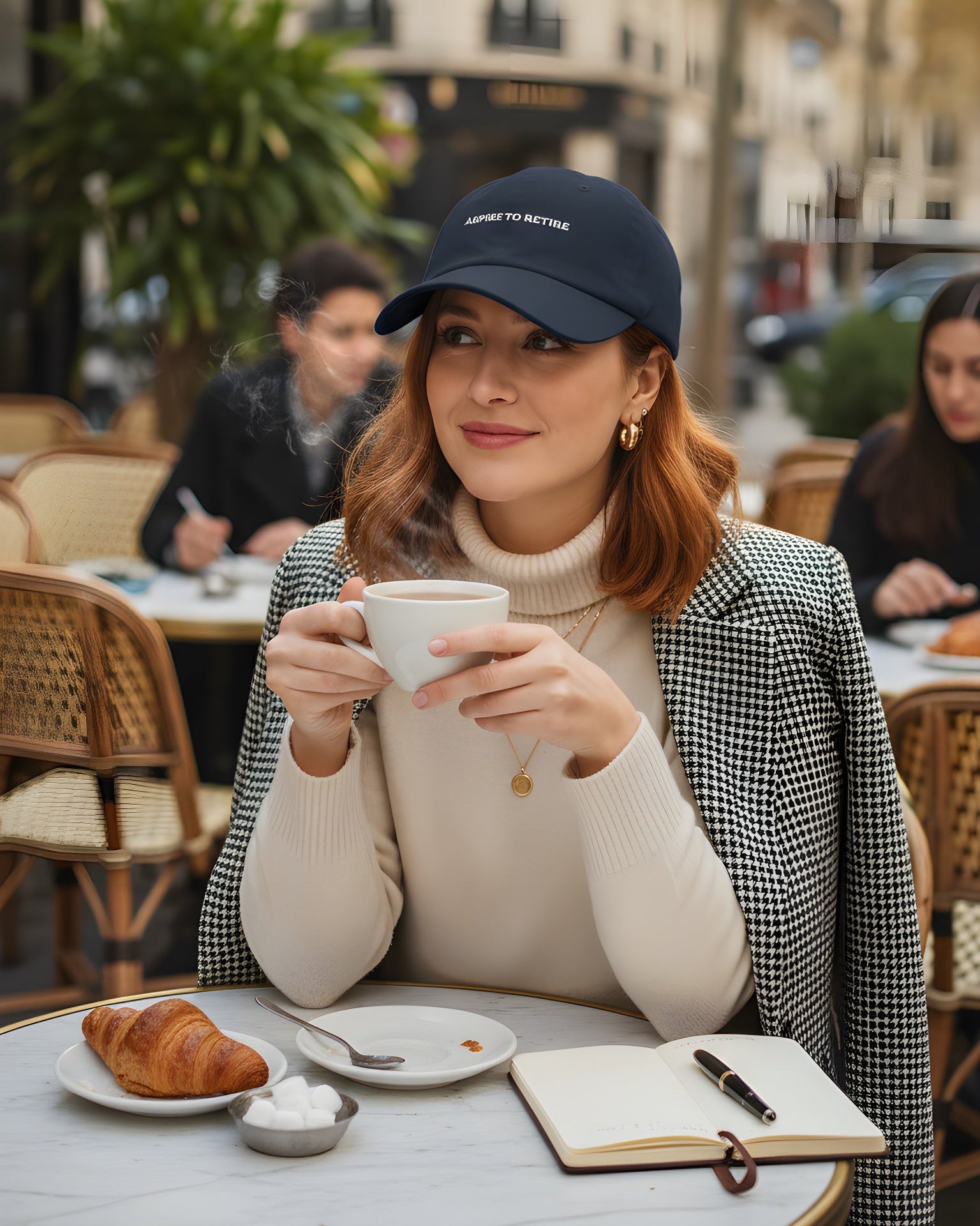 Woman sitting at an outdoor cafe holding a cup, with a city street in the background