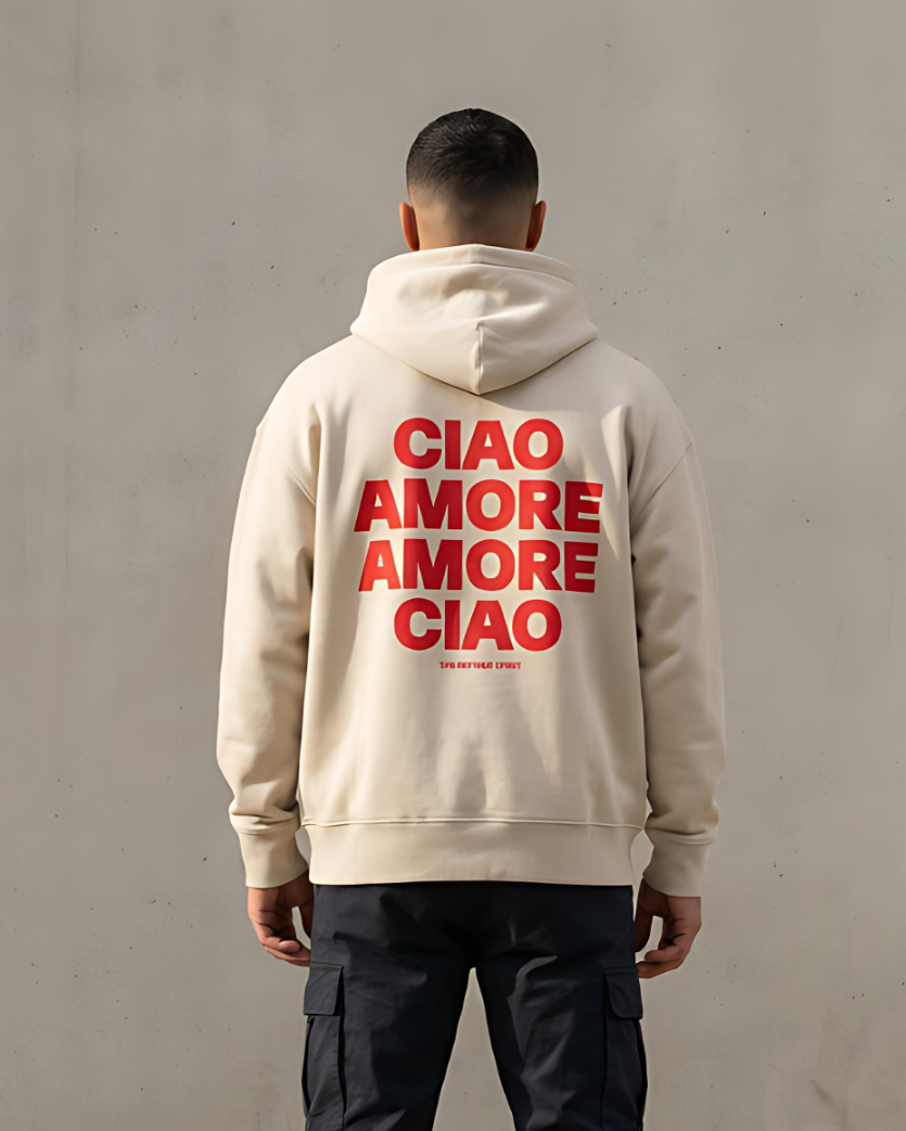 Person wearing a beige hoodie with red text on the back against a plain wall.