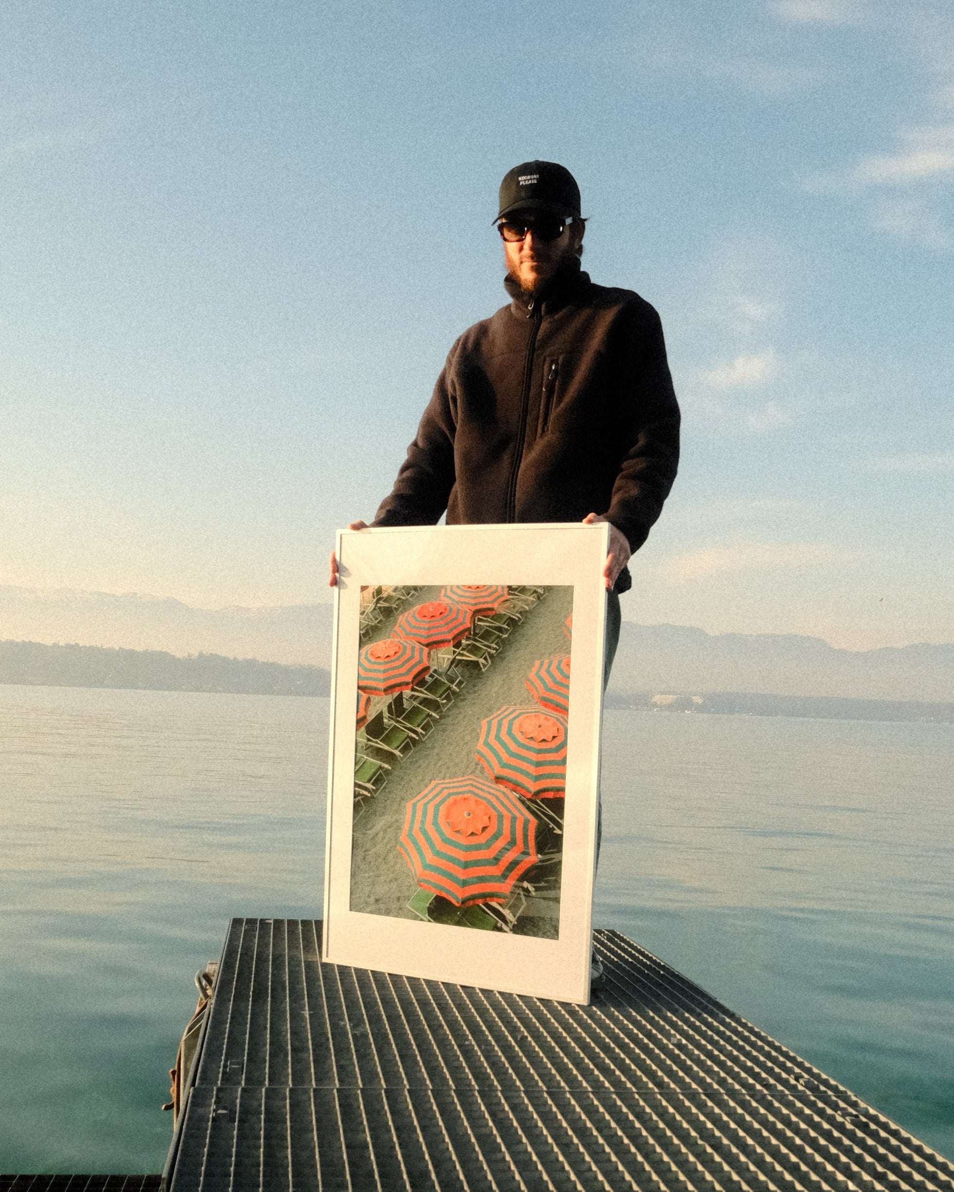 Person holding a framed picture of a sunset over water on a bridge