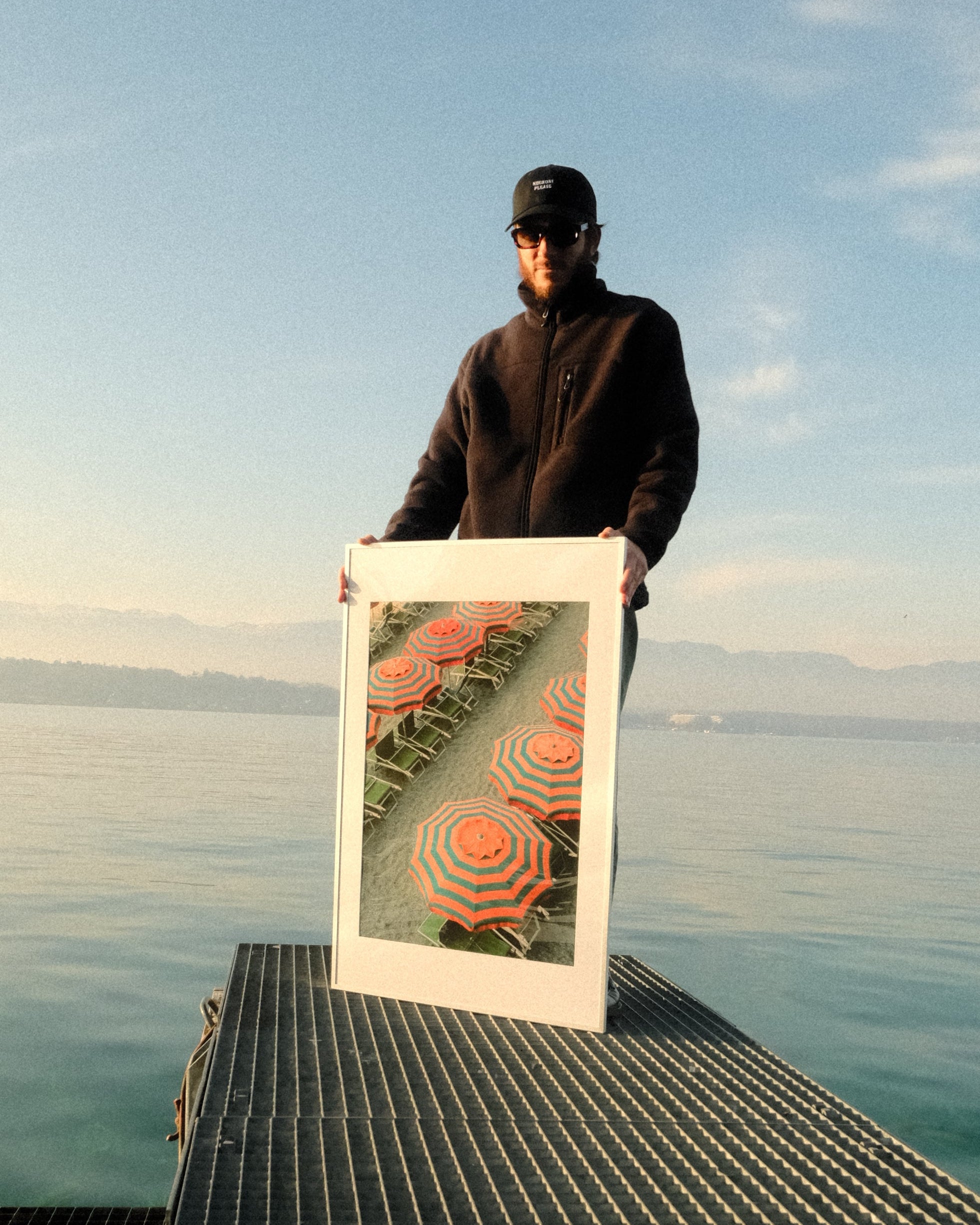 Person holding a framed picture of a sunset over water on a bridge