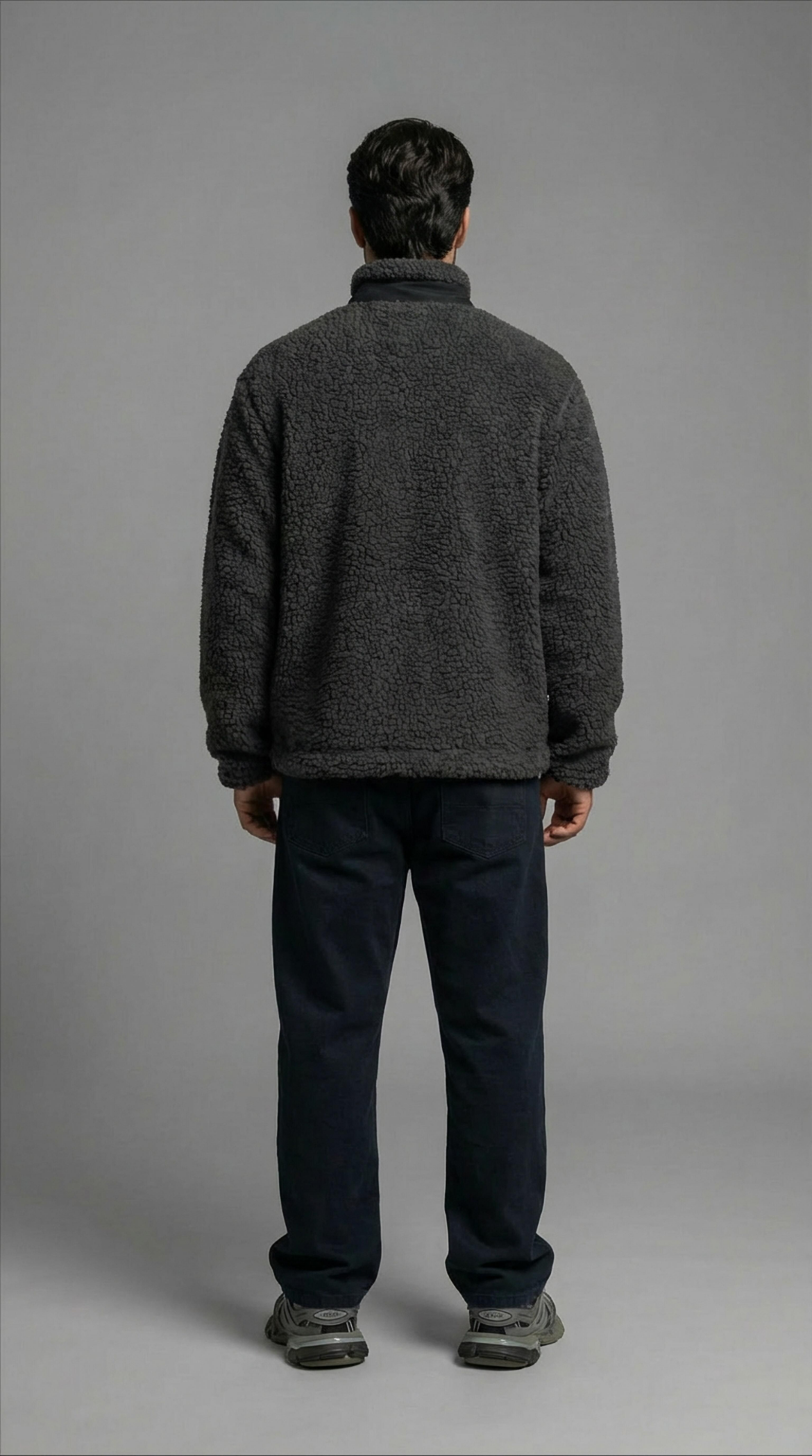 Person wearing a dark gray fleece jacket and pants on a plain background