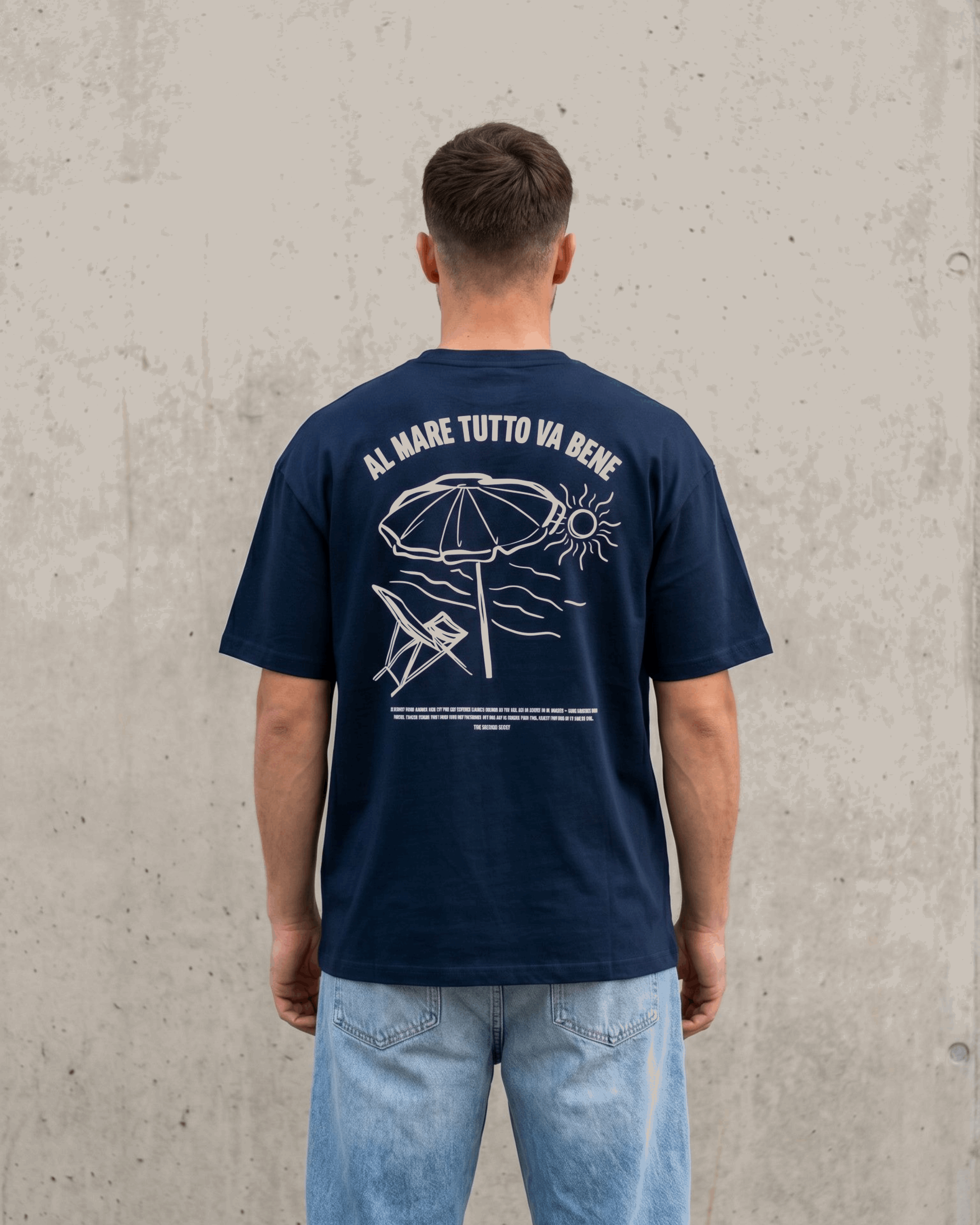 Person wearing a navy blue t-shirt with white graphics and text, standing against a concrete wall.