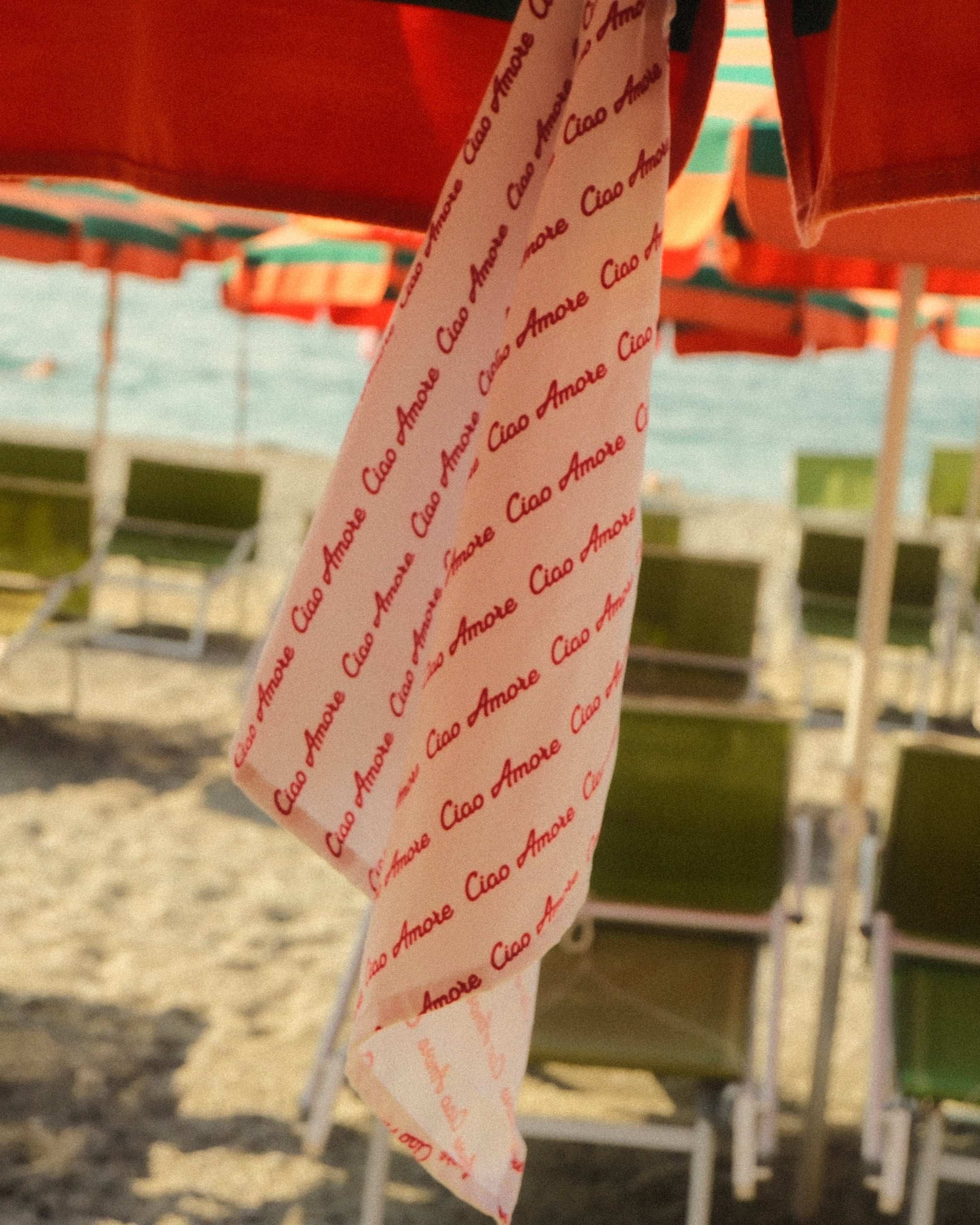 Beach scene with green chairs and red umbrellas, towel with text draped over chair.
