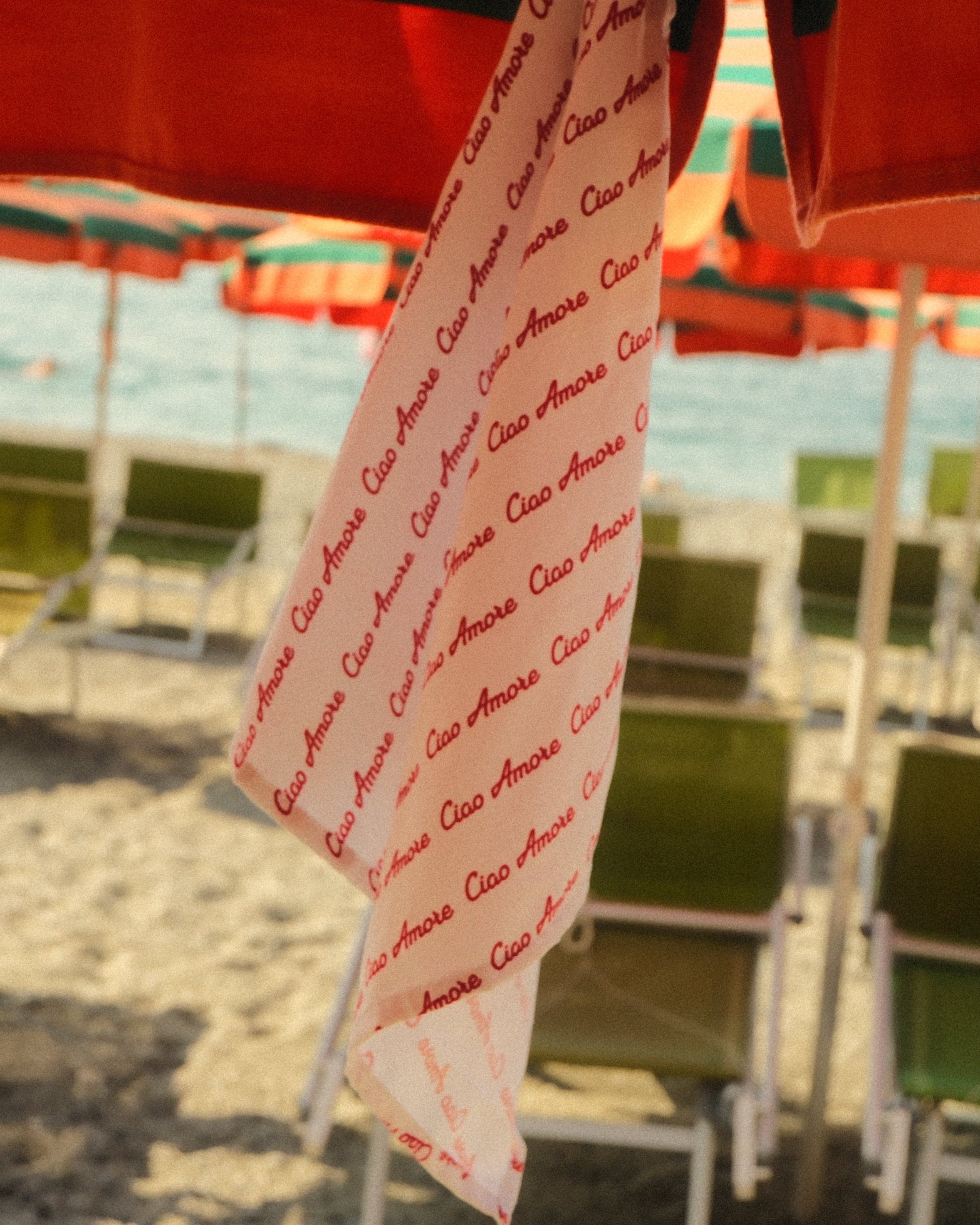 Beach scene with green chairs and red umbrellas, towel with text draped over chair.