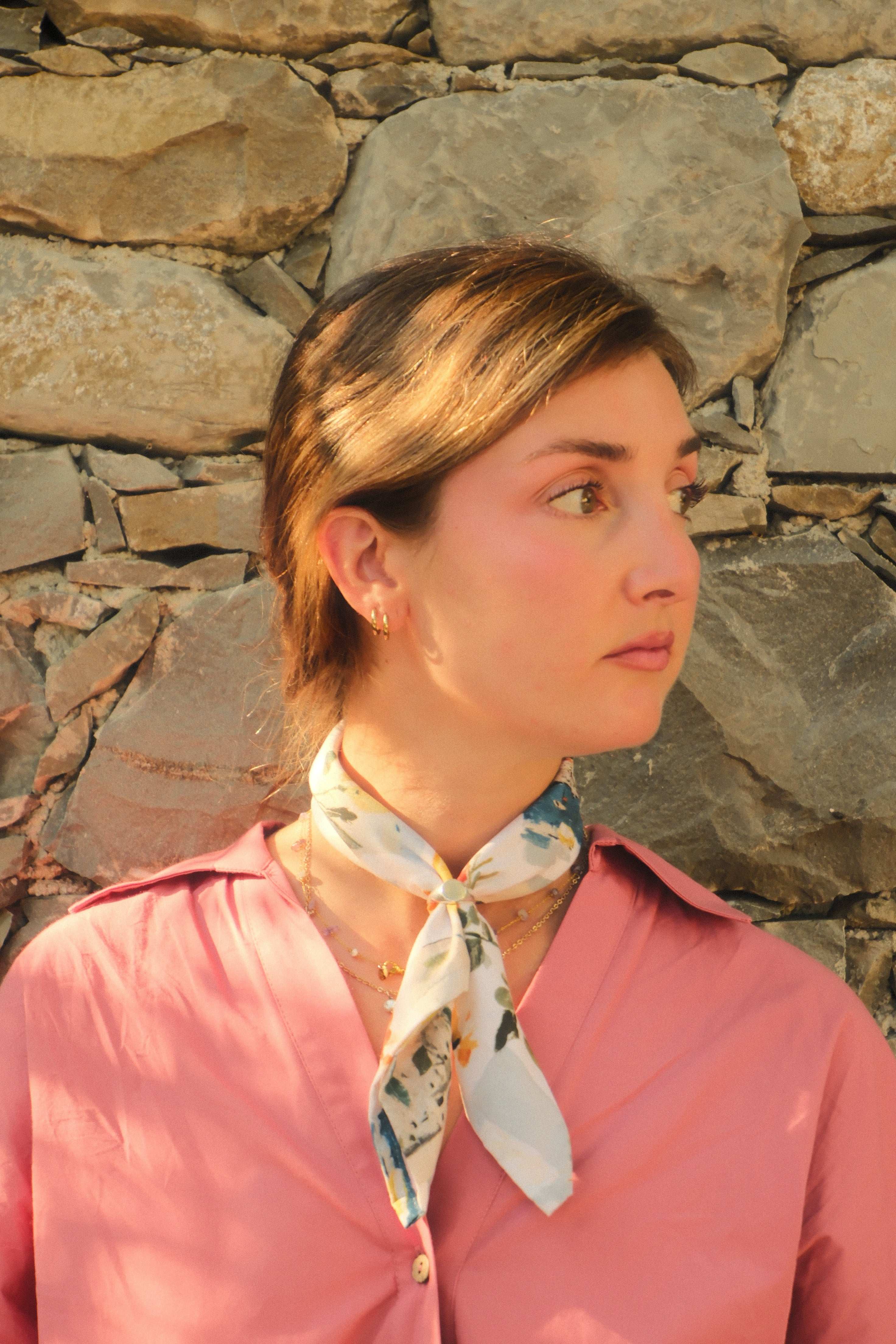 Woman wearing a pink shirt and floral scarf against a stone wall