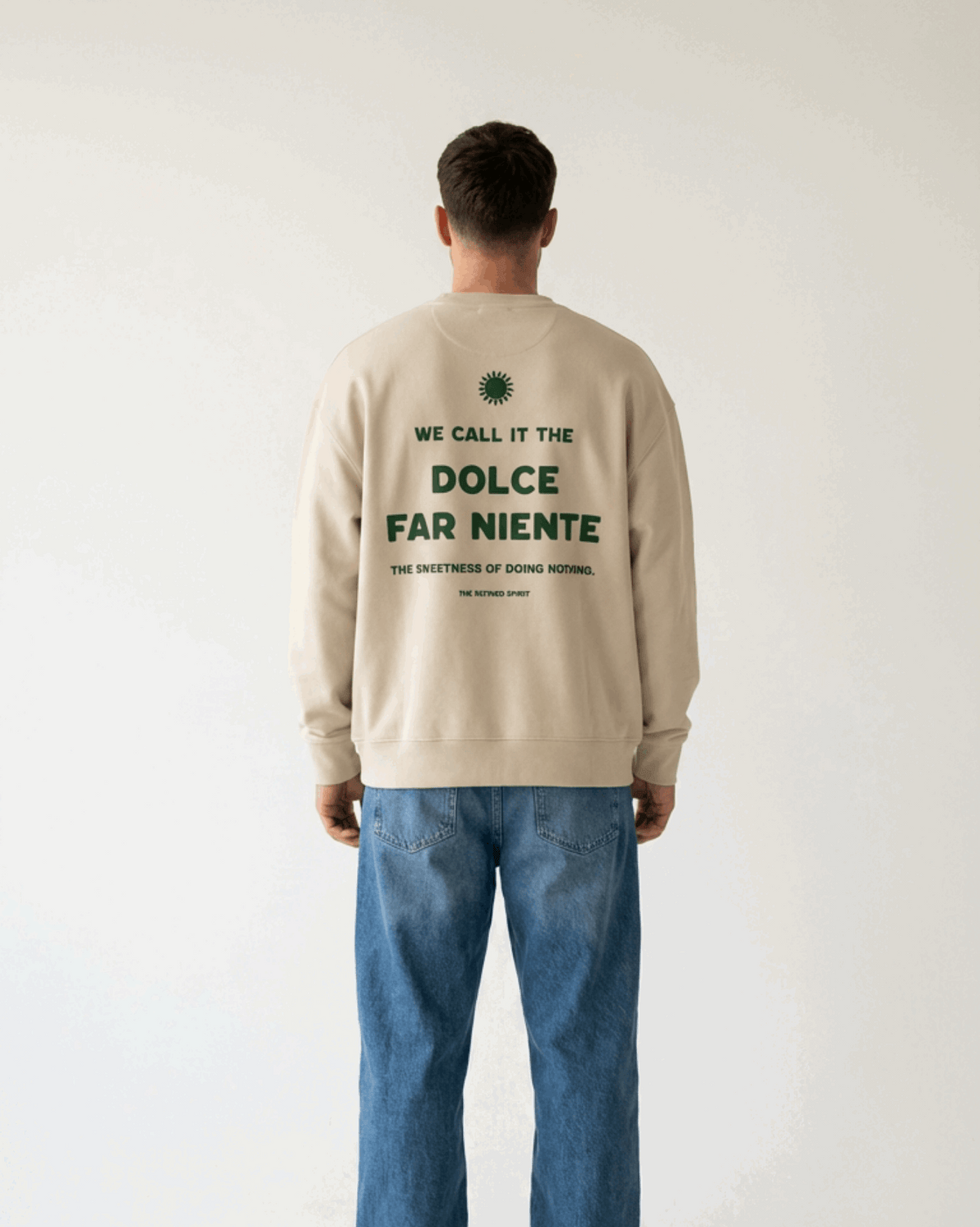 Person wearing a beige sweatshirt with text on the back, standing against a plain background