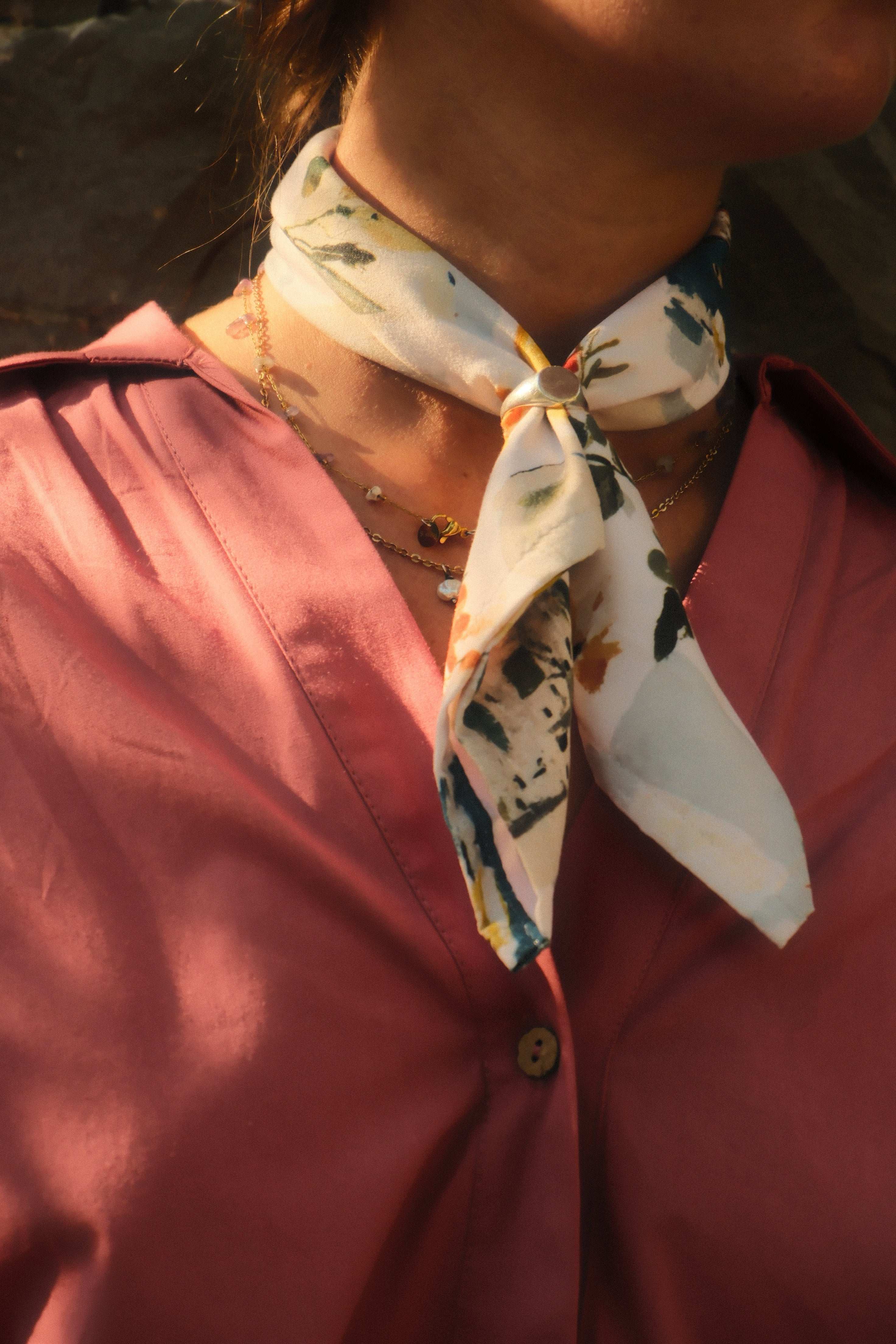 Close-up of a person wearing a pink shirt with a floral scarf tied around their neck.