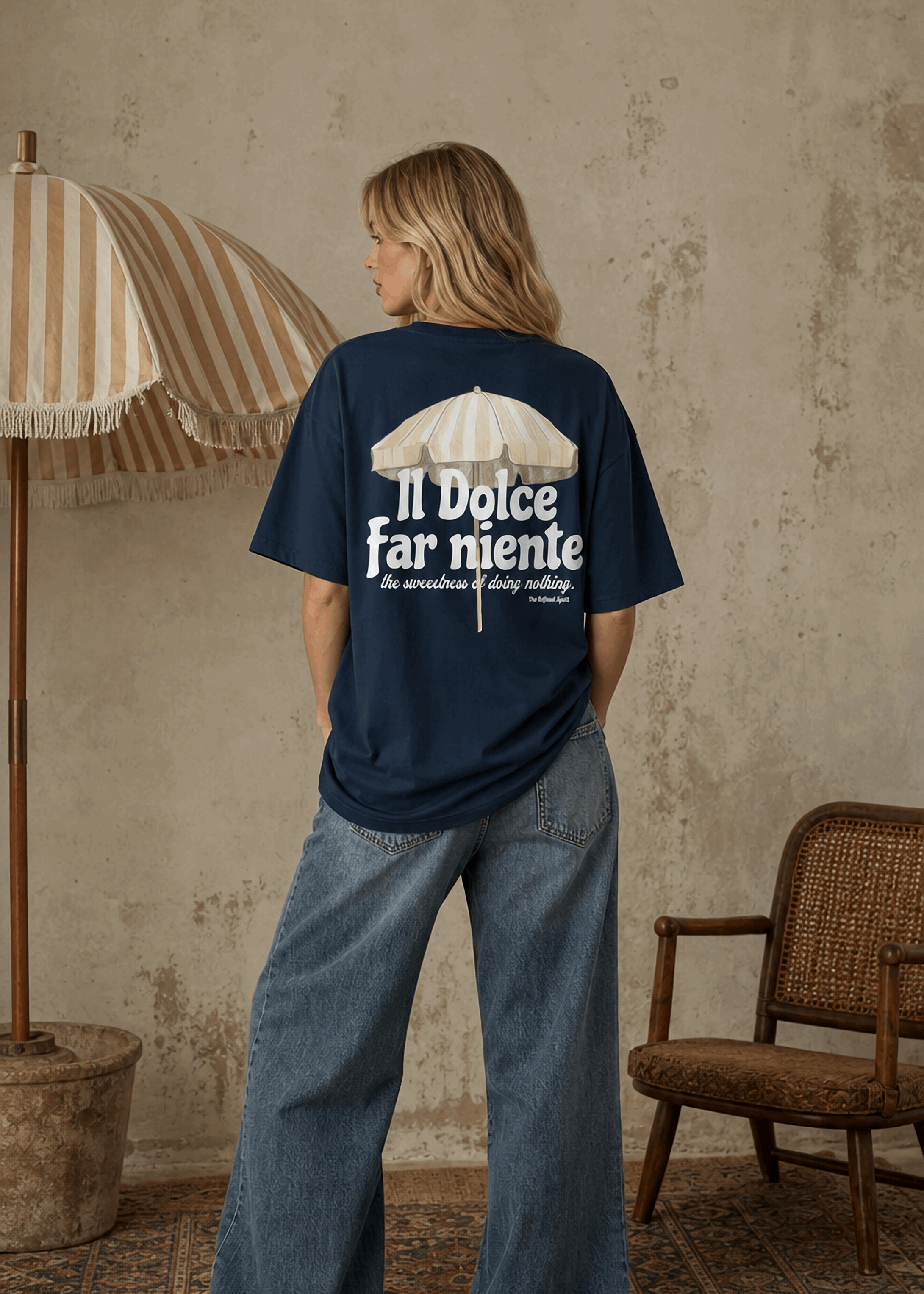 Person wearing a navy blue t-shirt with text and graphic, standing in a room with a textured wall, chair, and umbrella.