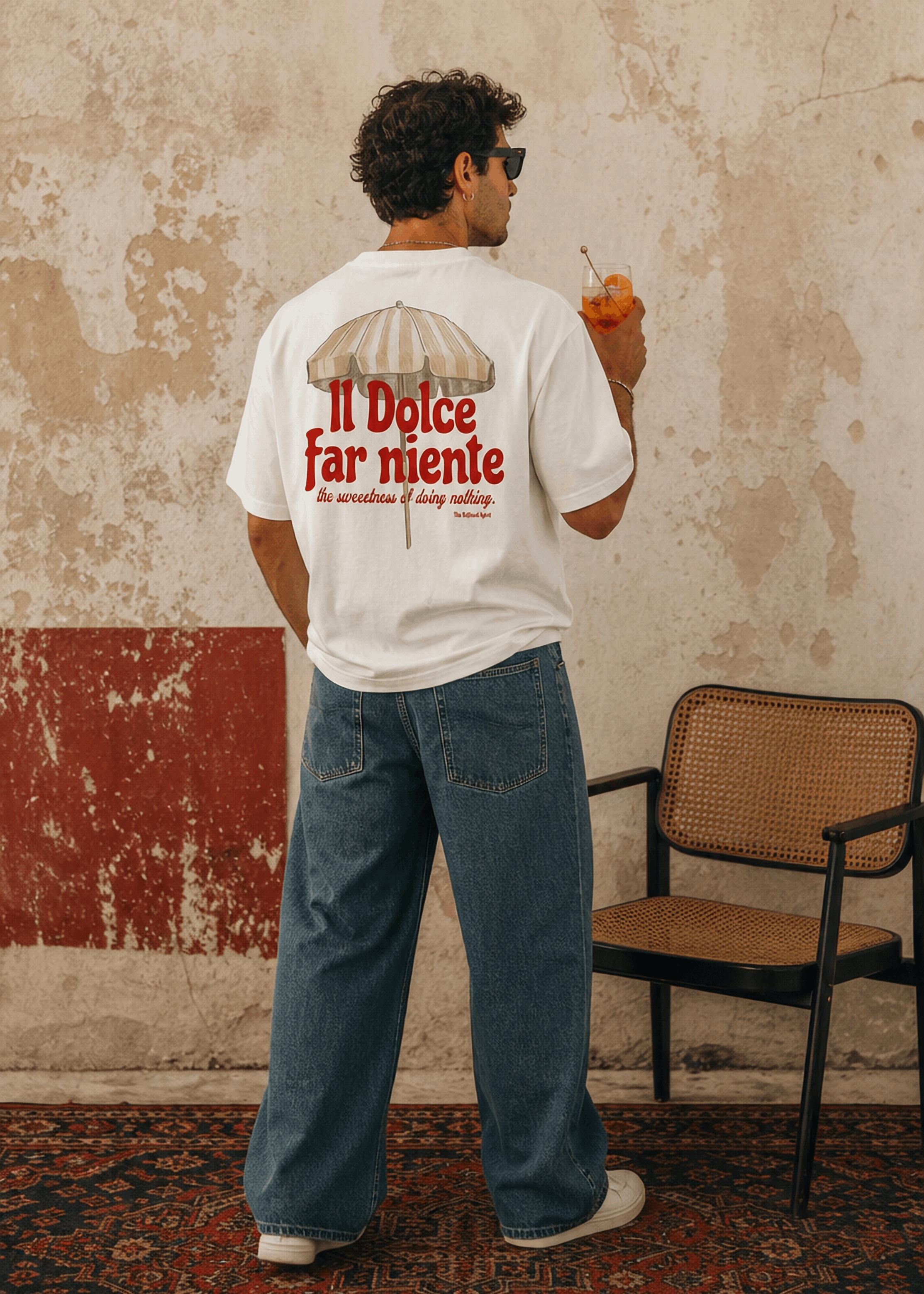 Person wearing a white t-shirt with text and graphics, standing in a room with a textured wall and chair.