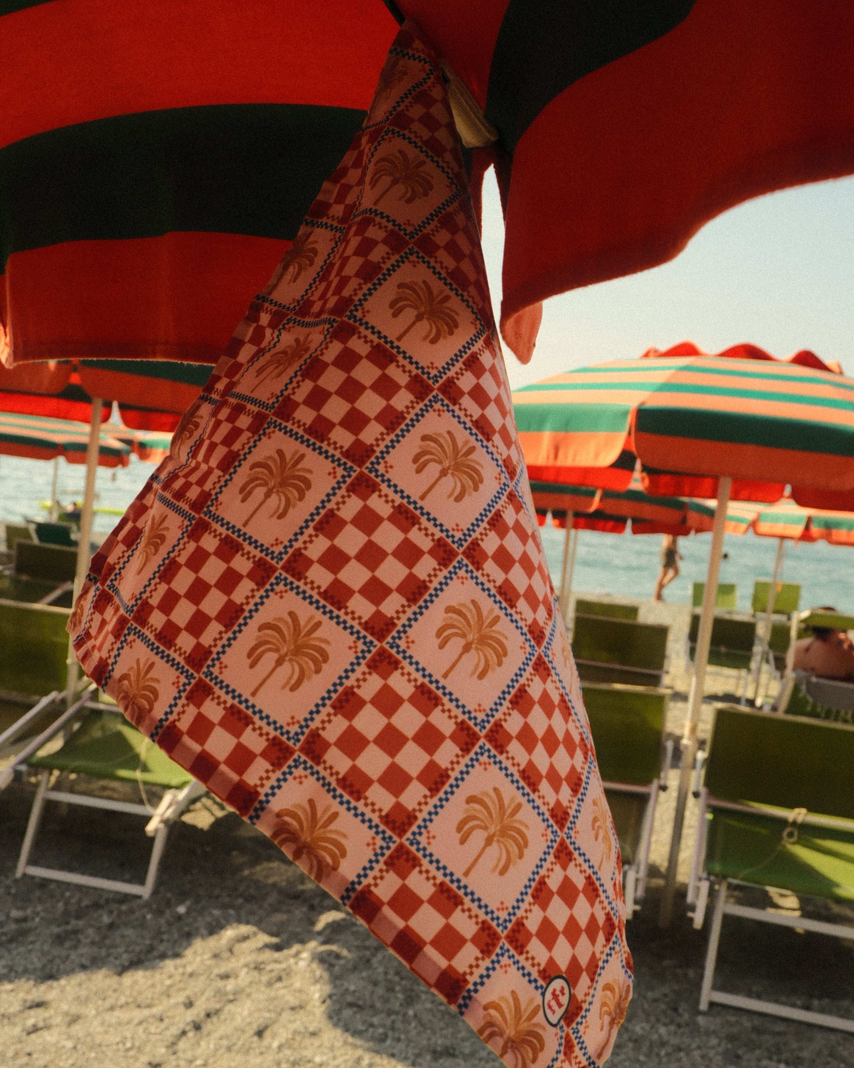 Checkered bag with palm tree pattern on a beach with umbrellas and chairs in the background