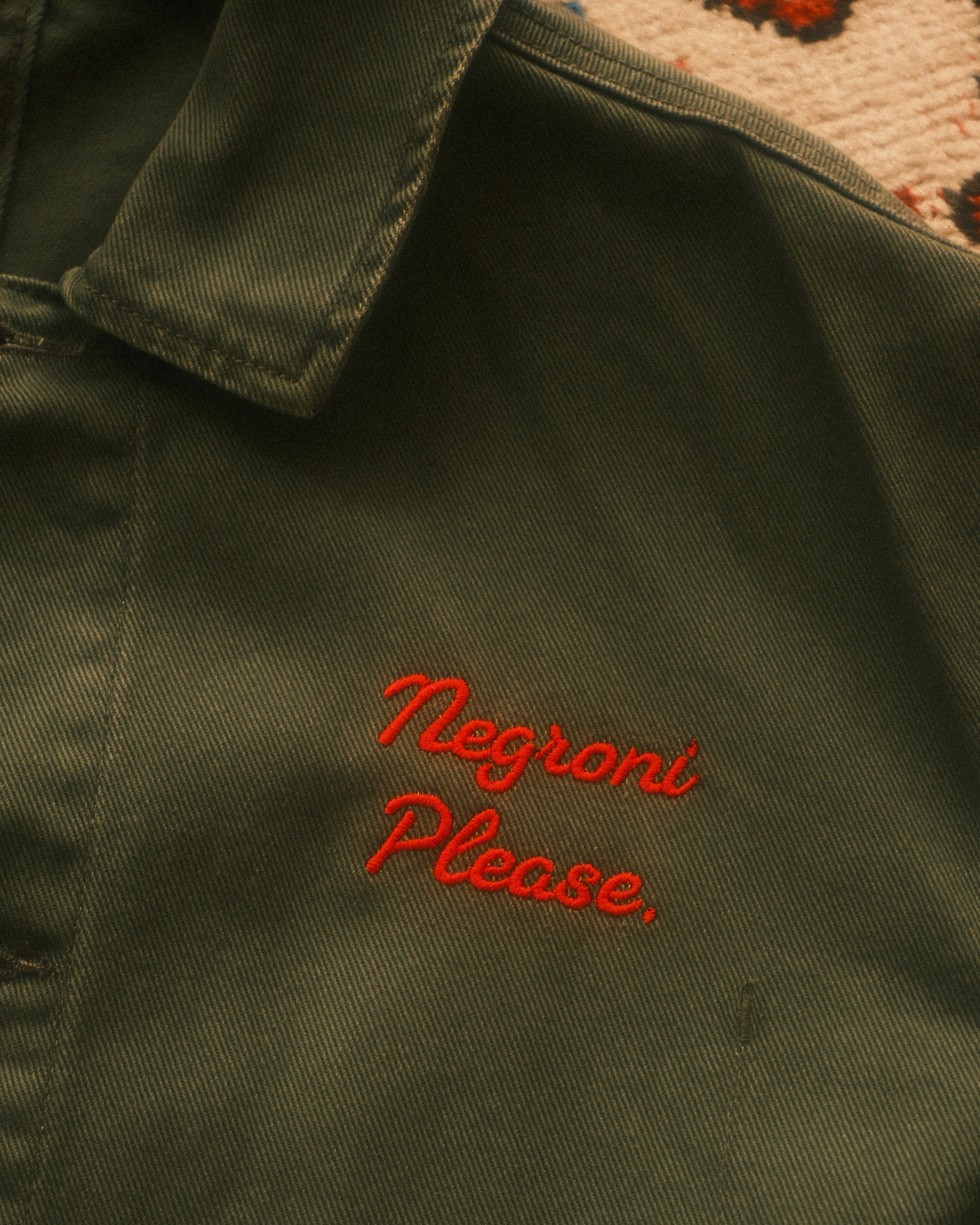 Green jacket with 'Negroni Please' embroidery on a textured background