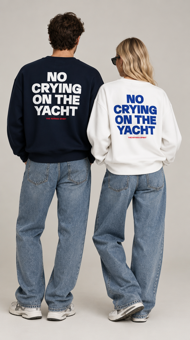 Two models from behind wearing matching oversized sweatshirts with the slogan 'NO CRYING ON THE YACHT' printed in large letters on the back. The man wears a navy blue sweatshirt with white text, and the woman wears a white sweatshirt with blue text.