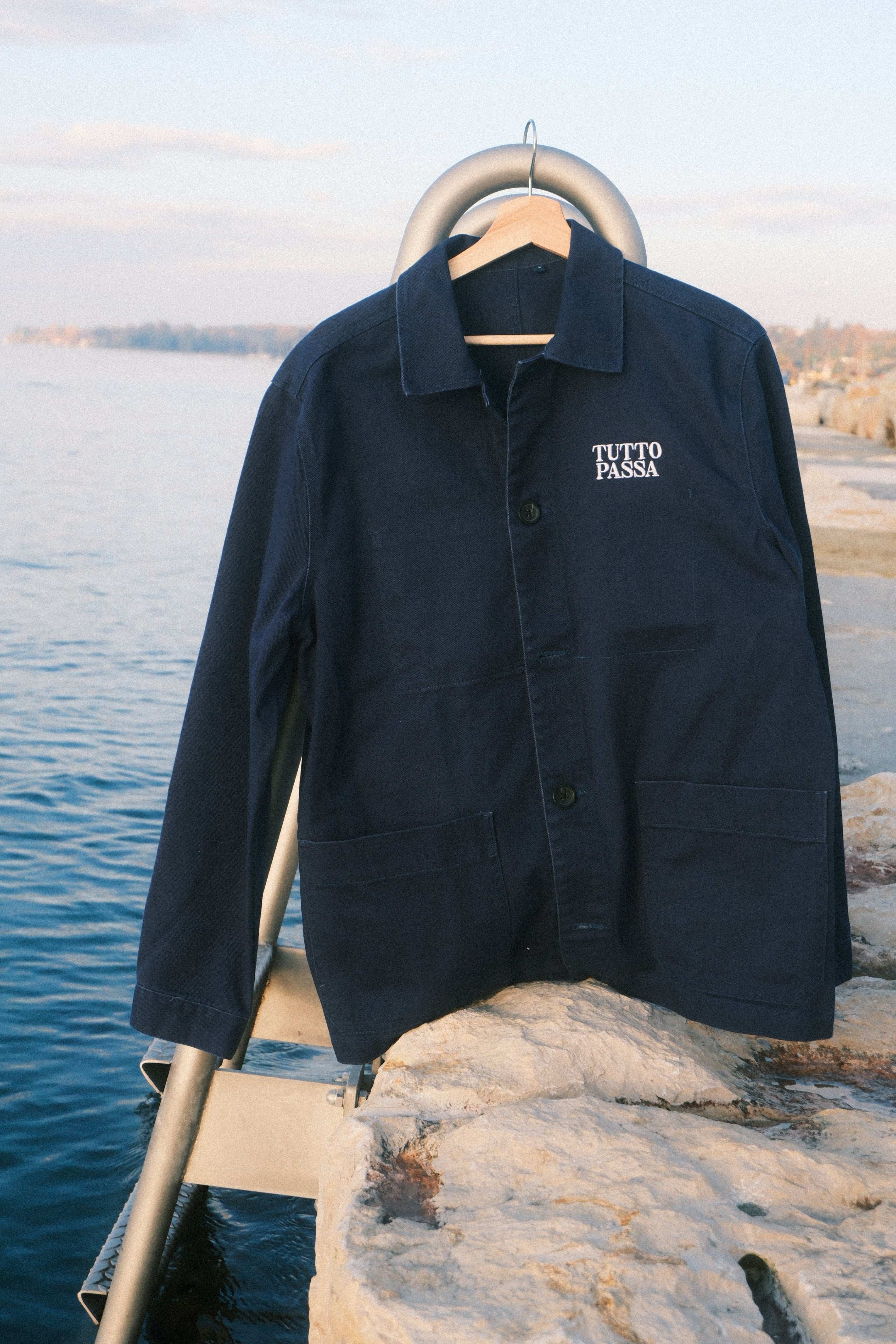 Blue jacket with tutto passa logo on a metal stand against a natural background