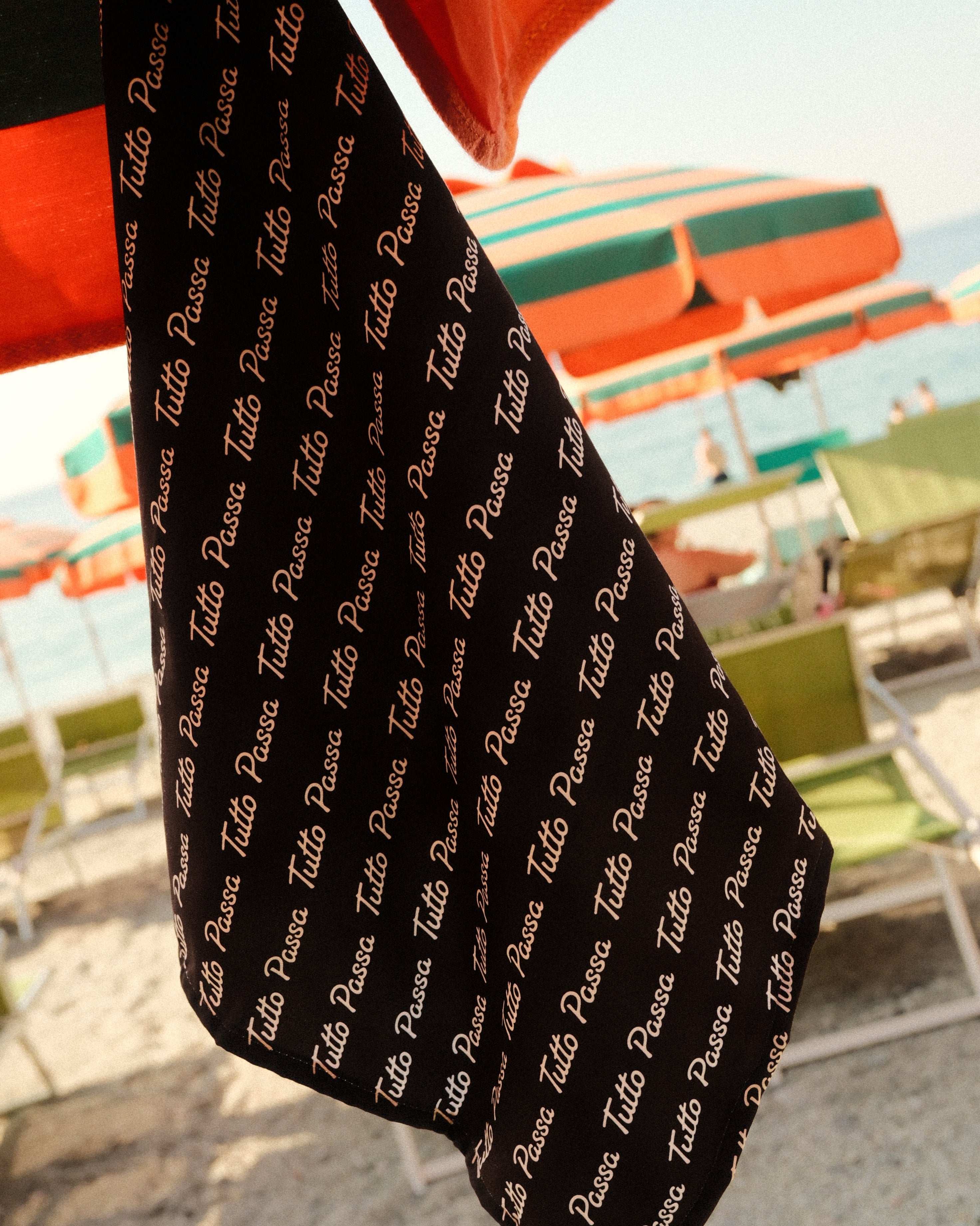 Black fabric with 'Tutto Passo' text in a beach setting