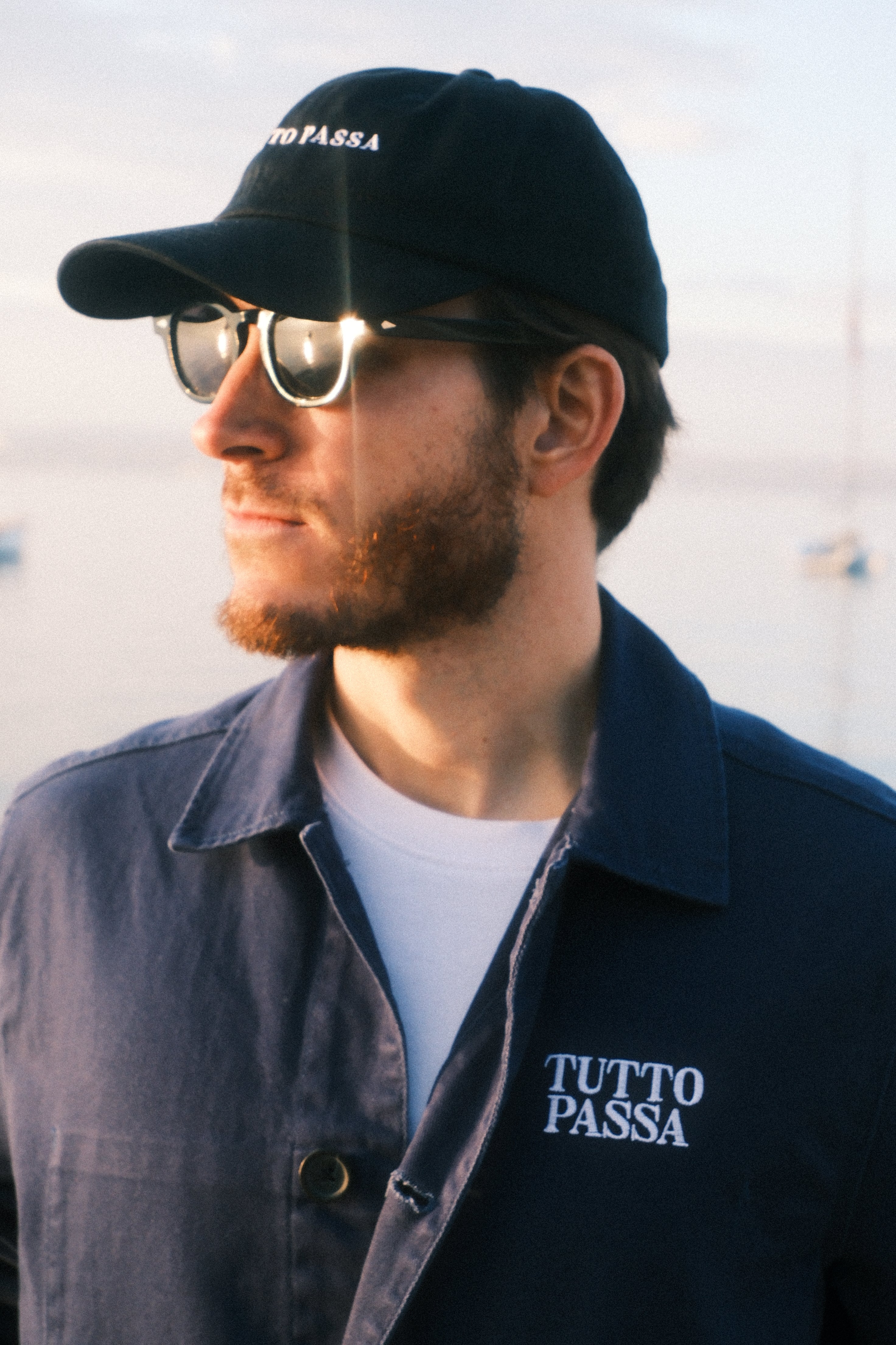 Man wearing a black cap and sunglasses with 'PASSE' branding, looking to the side.