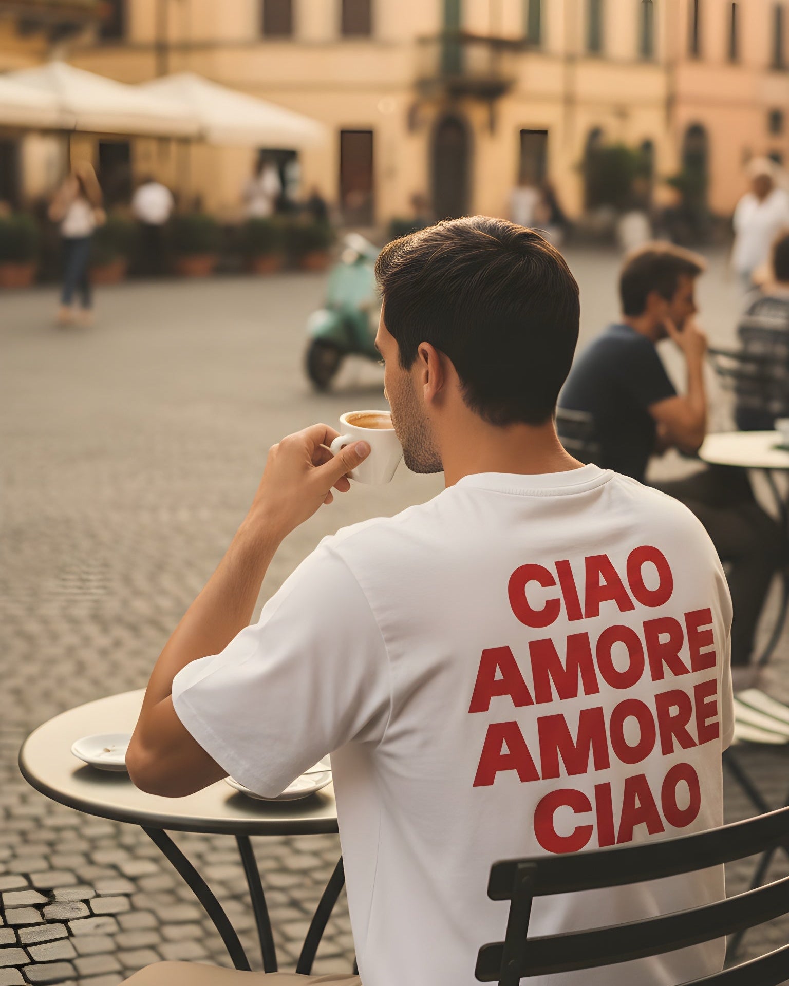 Man sitting on a bench in an Italian street, wearing a white t-shirt with red text.