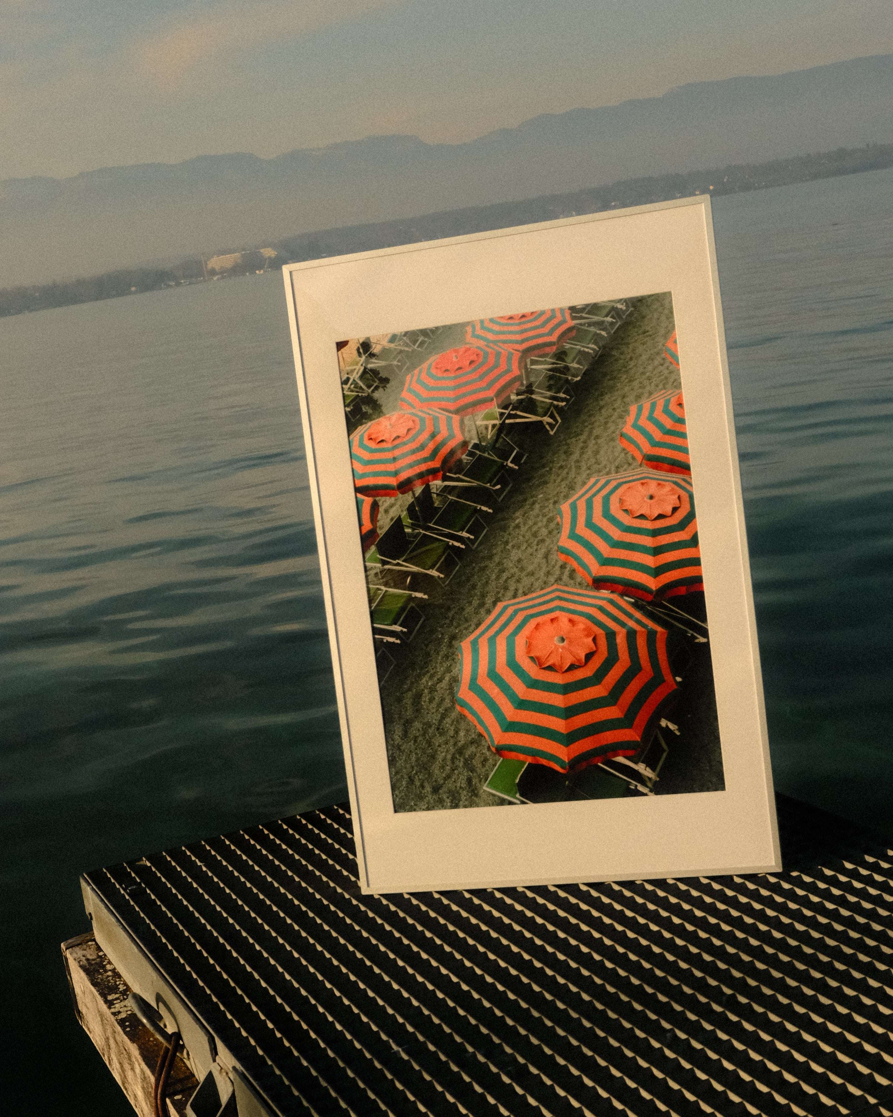 Framed picture of orange and green striped umbrellas on a grassy area, leaning against a textured wall.