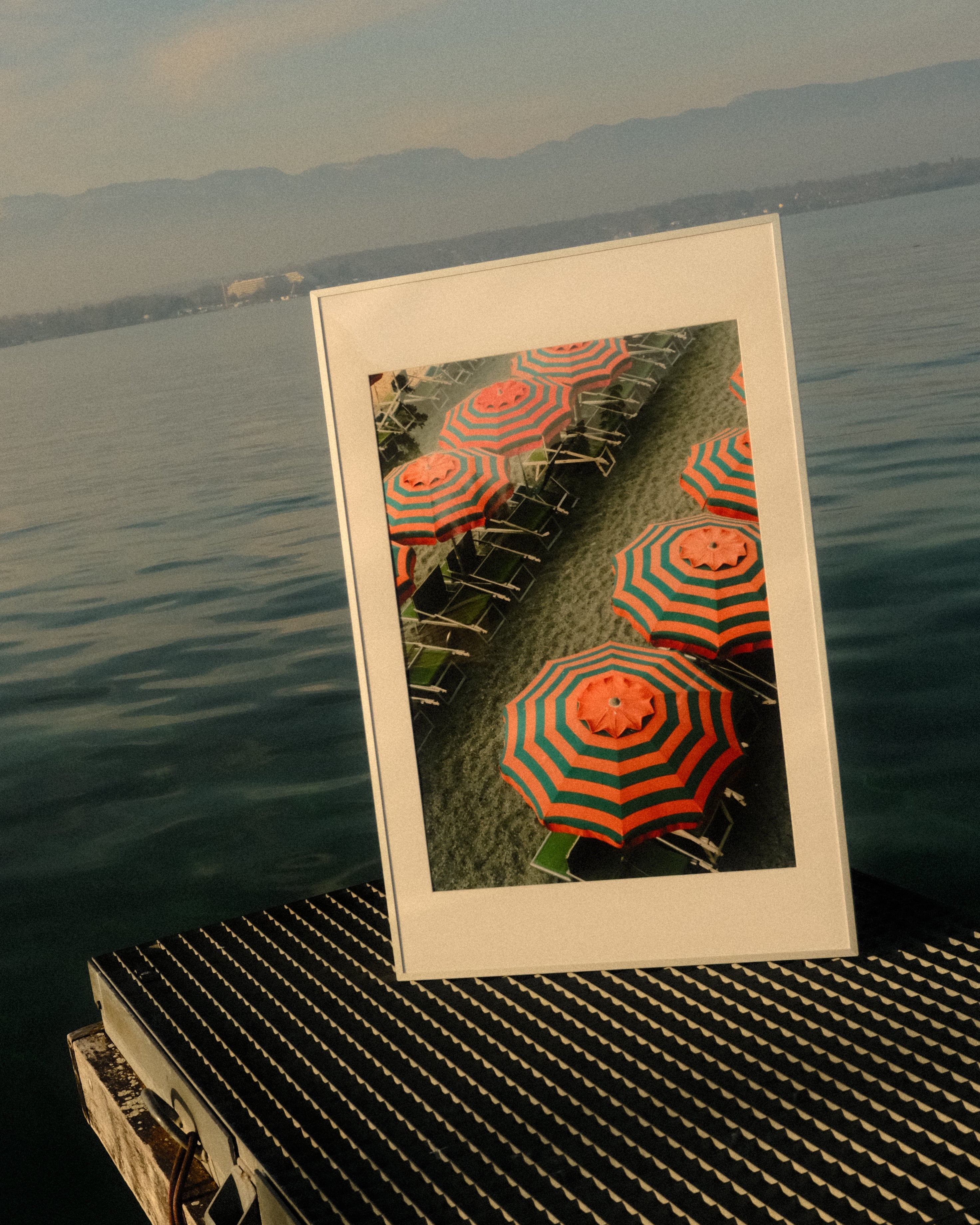 Framed picture of orange and green striped umbrellas on a grassy area, leaning against a textured wall.