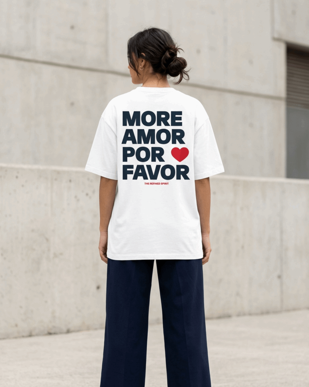 Person wearing a white t-shirt with text on the back, standing against a concrete wall.