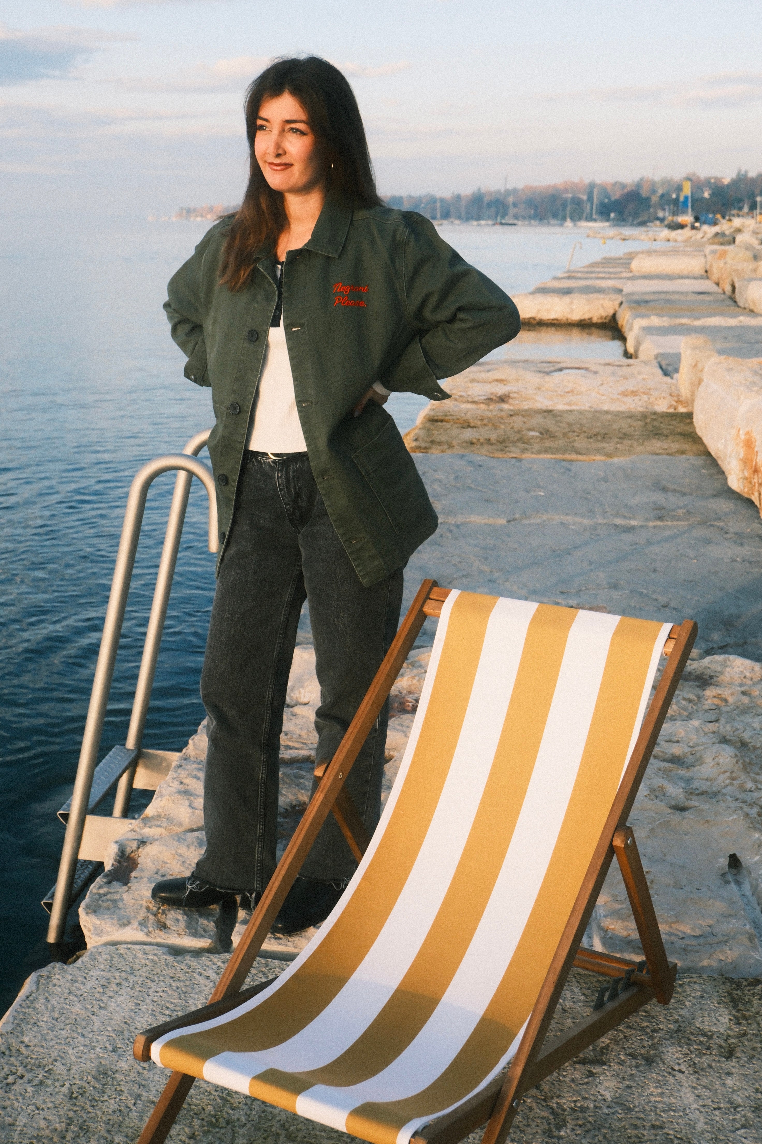Woman standing by a deck chair on a dock by water