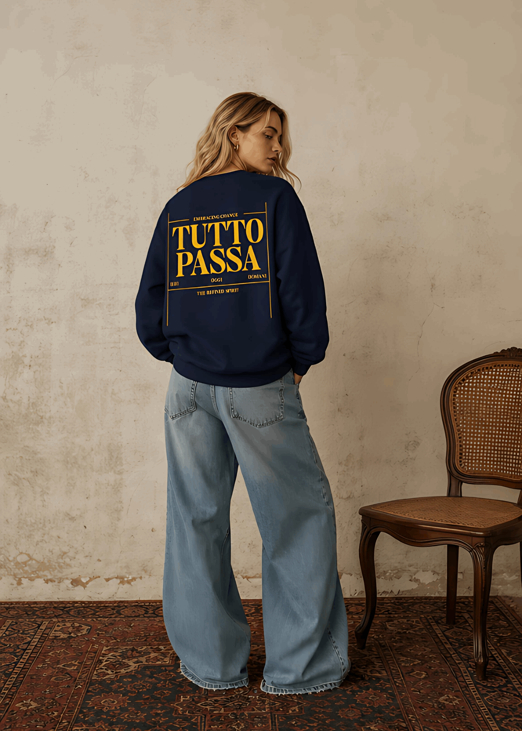 Person wearing a navy blue sweatshirt with 'TUTTO PASSA' text in yellow, standing against a textured wall.