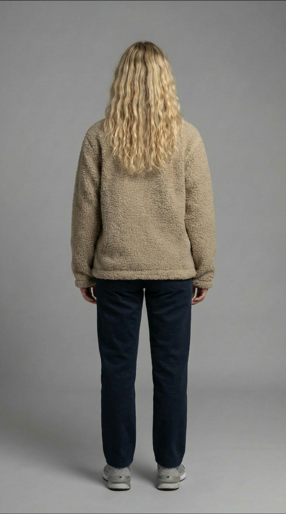 Person wearing a beige sweater and dark pants on a gray background