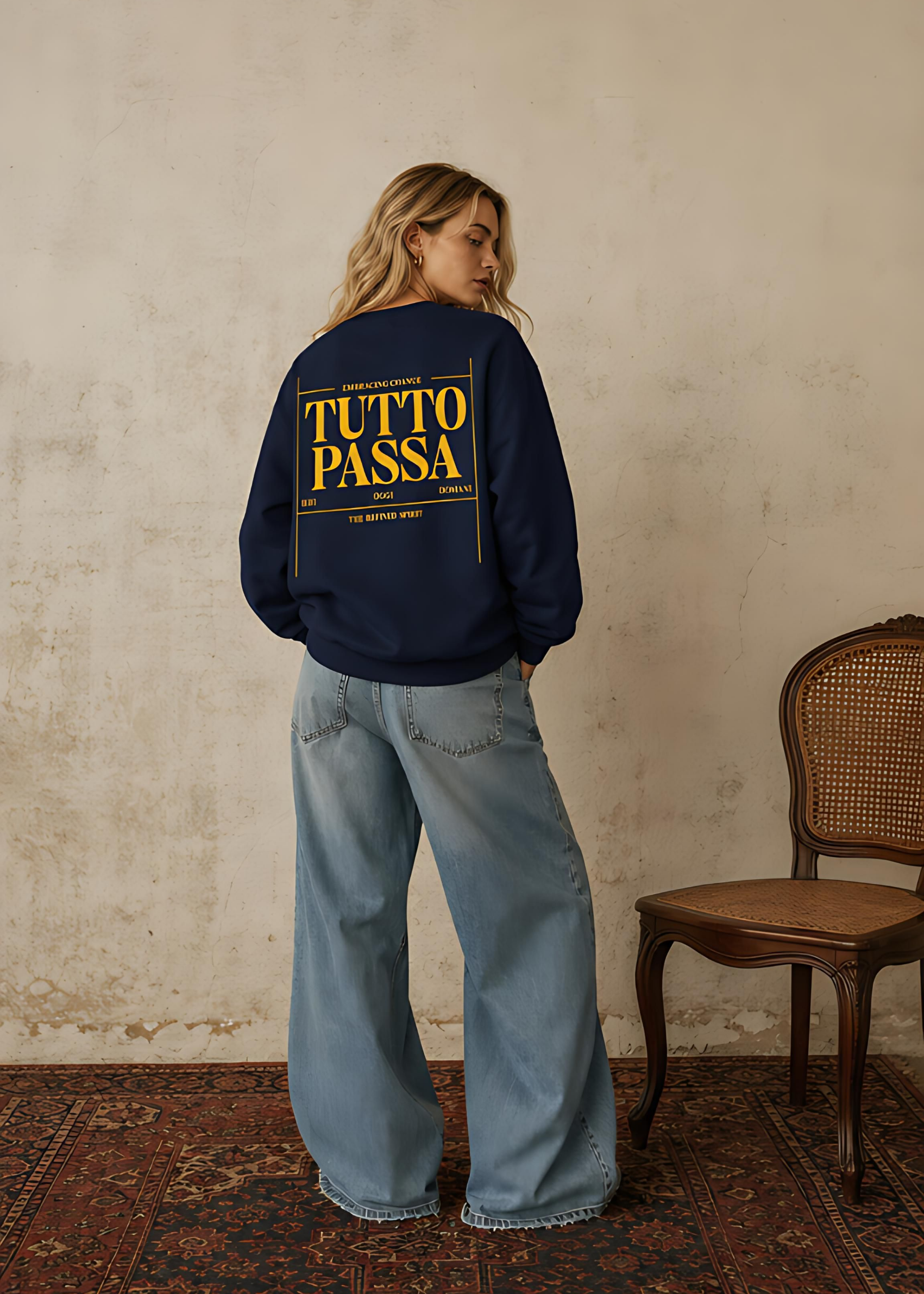 Person wearing a navy blue sweatshirt with 'TUTTO PASSA' text in yellow, standing against a textured wall.
